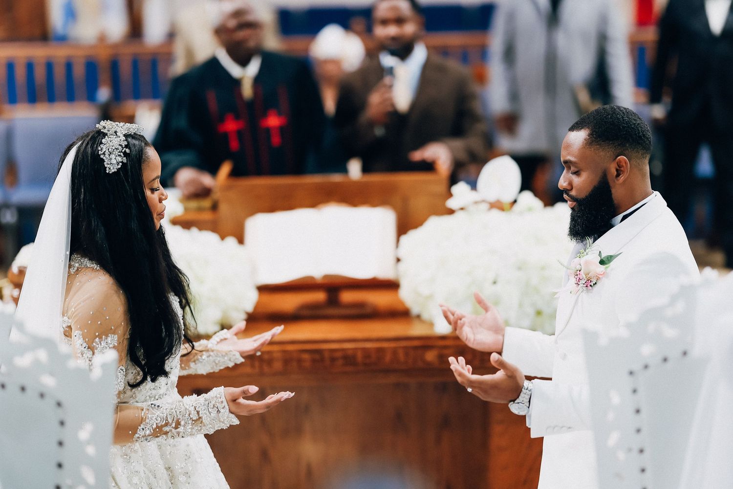 Bride and groom exchange vows at elegant church wedding ceremony with white floral arrangements.