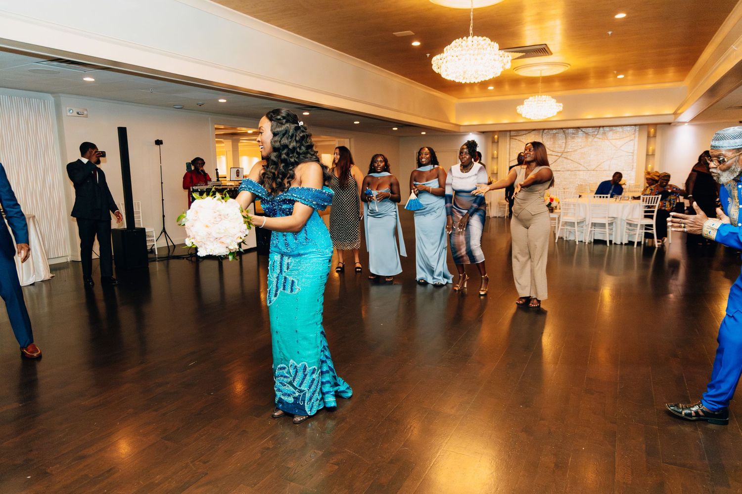 Bride in blue African print gown dancing with bridesmaids at wedding reception.