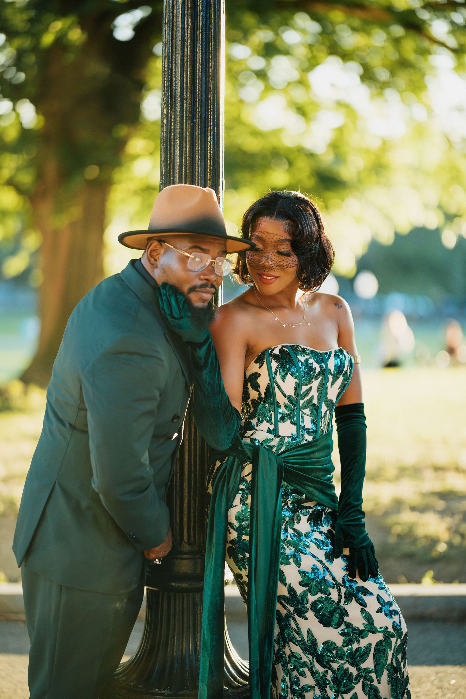 Stylish couple in emerald green attire sharing a tender moment by a park lamppost.