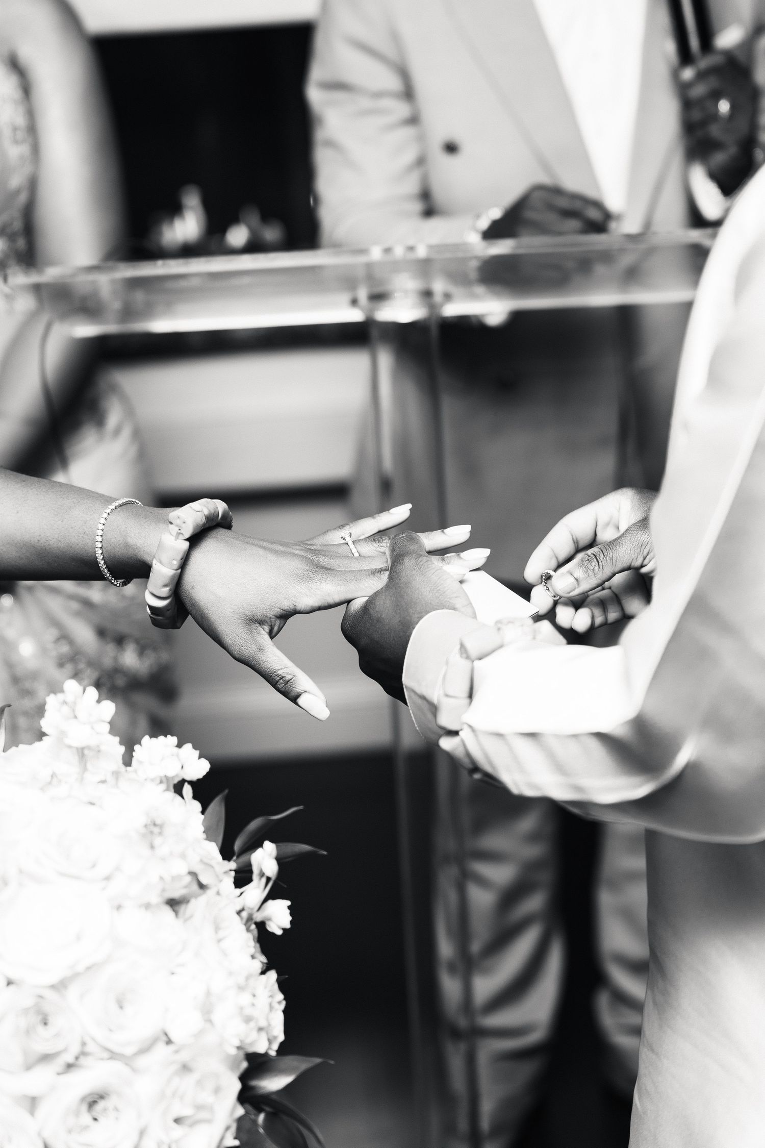 Black and white photo of a groom placing a wedding ring on the bride's finger during a ceremony.