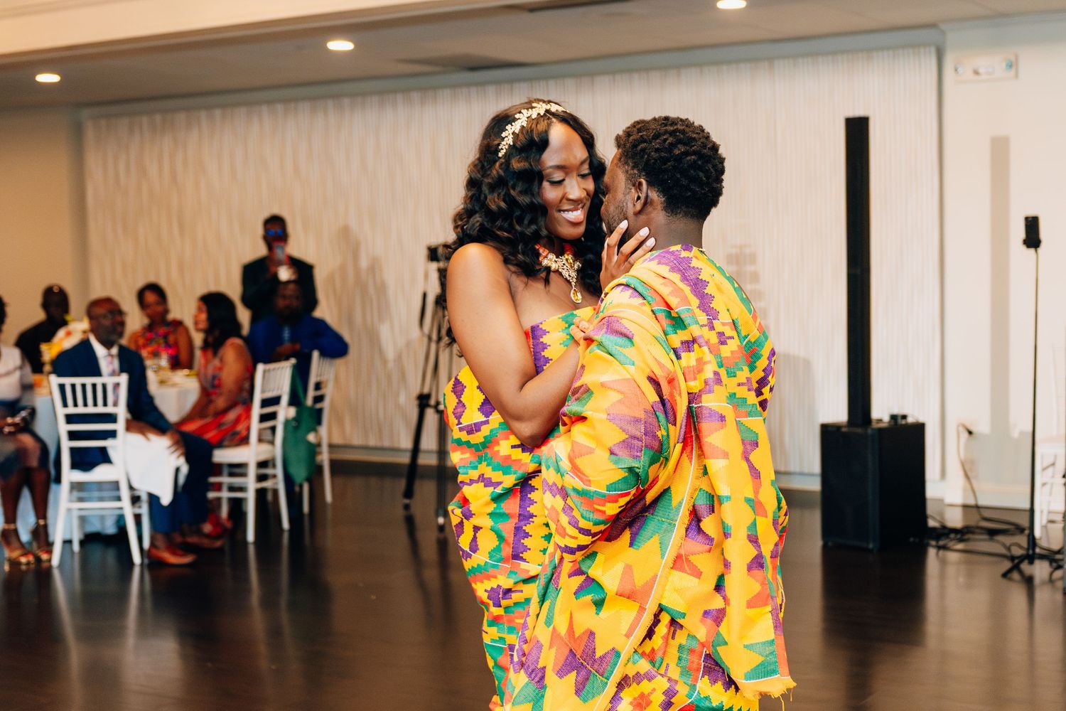Couple dancing in colorful Kente cloth outfits at a traditional African wedding reception.