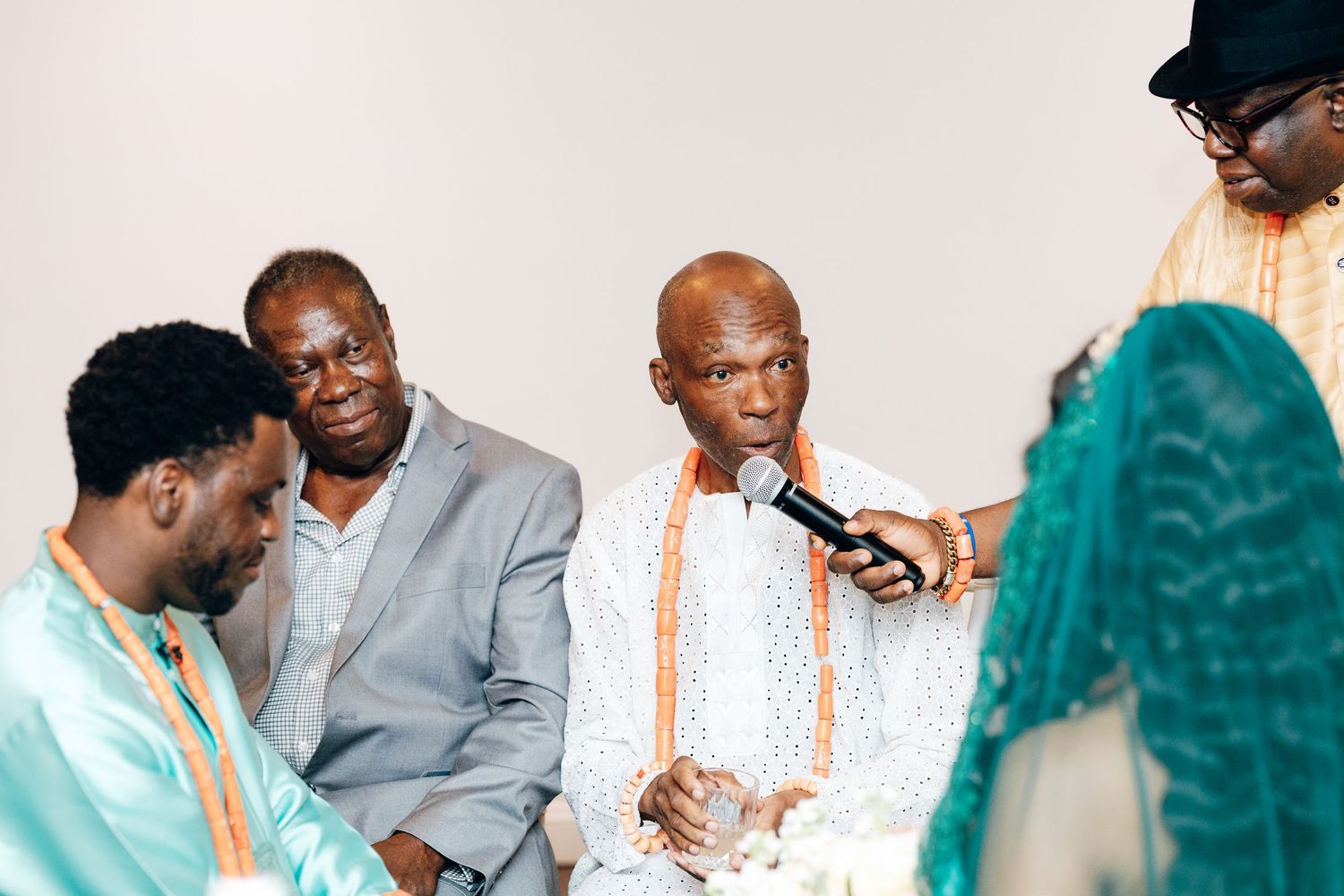 Group of men in traditional African attire gather around groom during wedding ceremony.