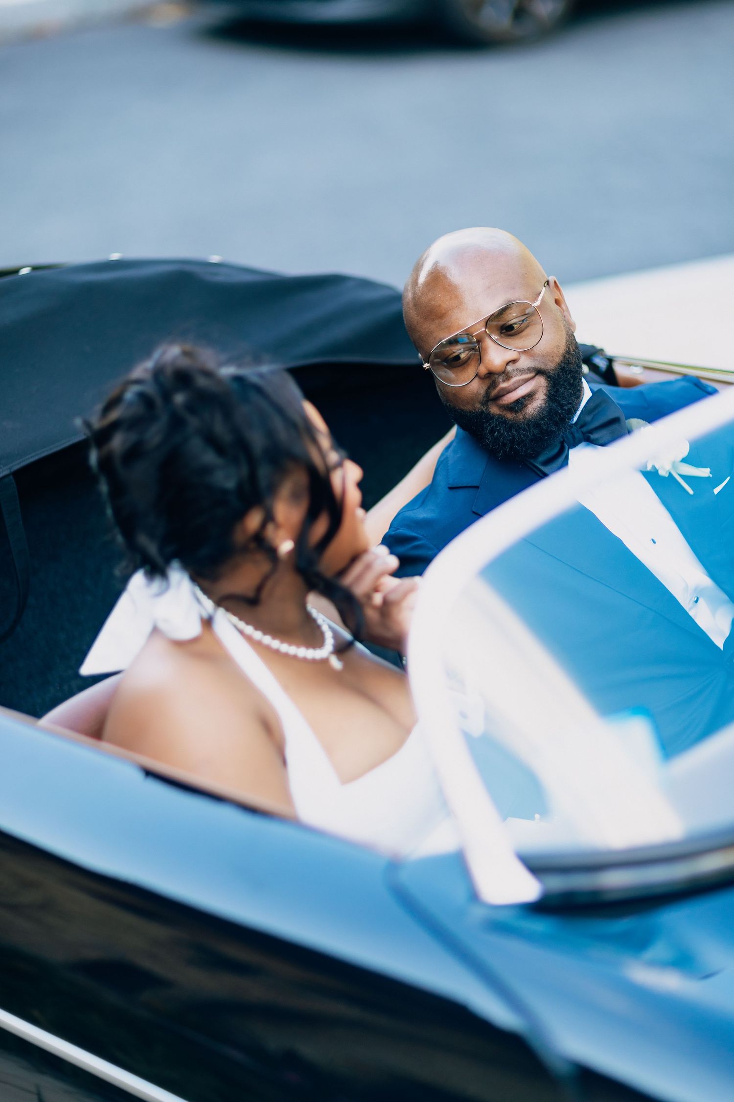Black bride and groom sharing an intimate moment inside a classic vintage convertible on their wedding day.