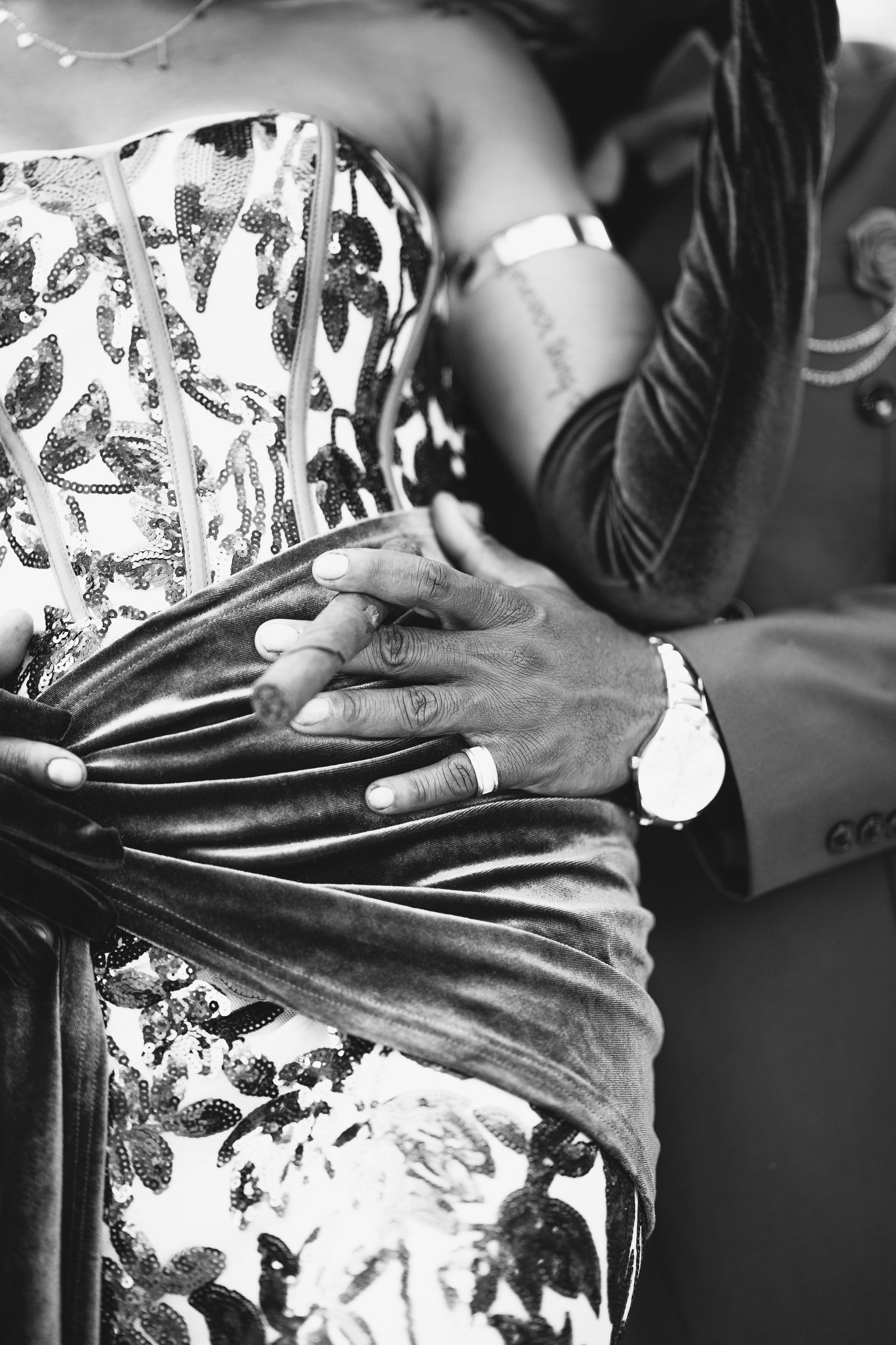 Black and white close-up of couple holding hands with wedding rings and watch.