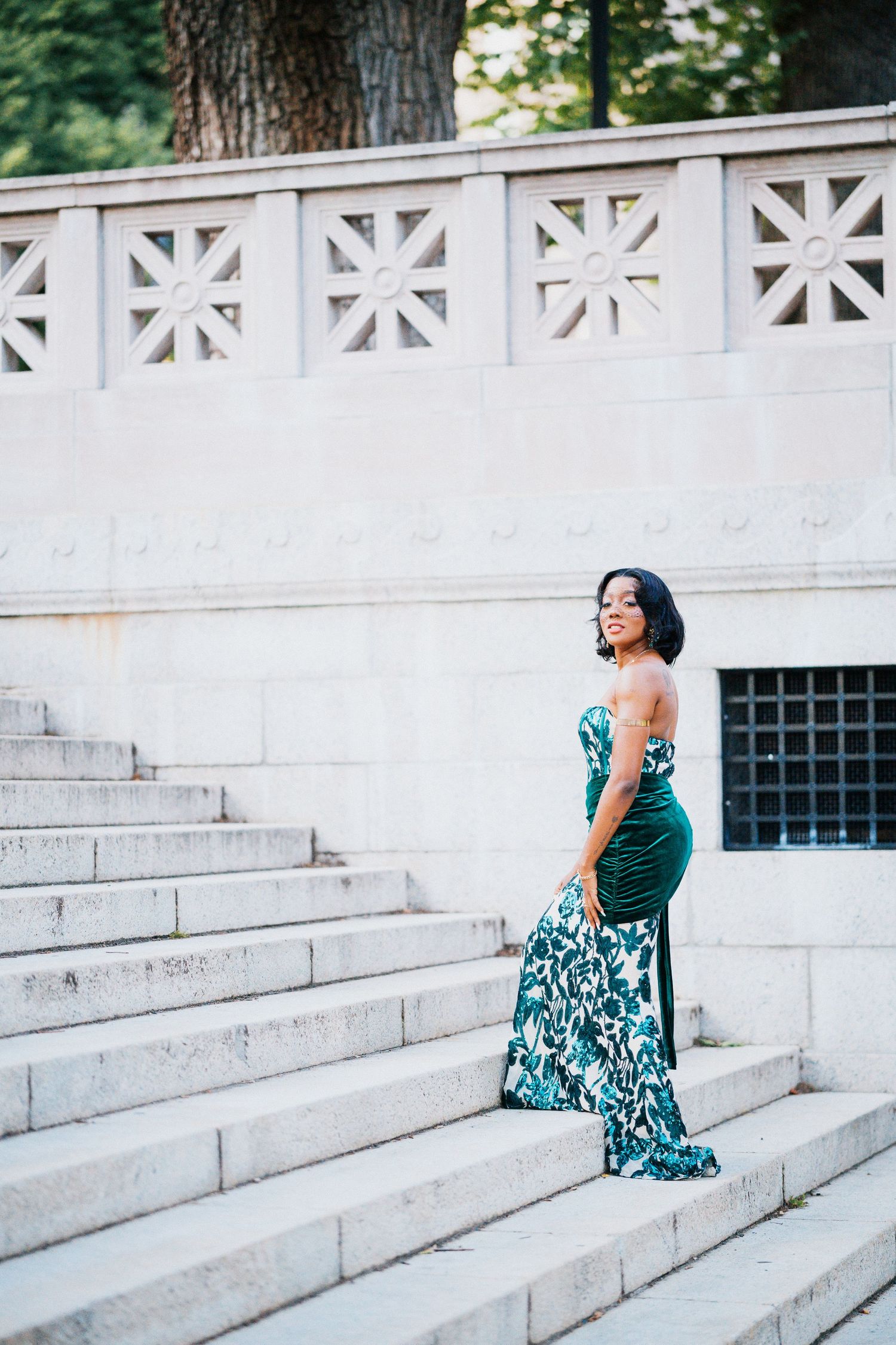 Woman in elegant green floral strapless gown posing on marble steps at an outdoor monument.