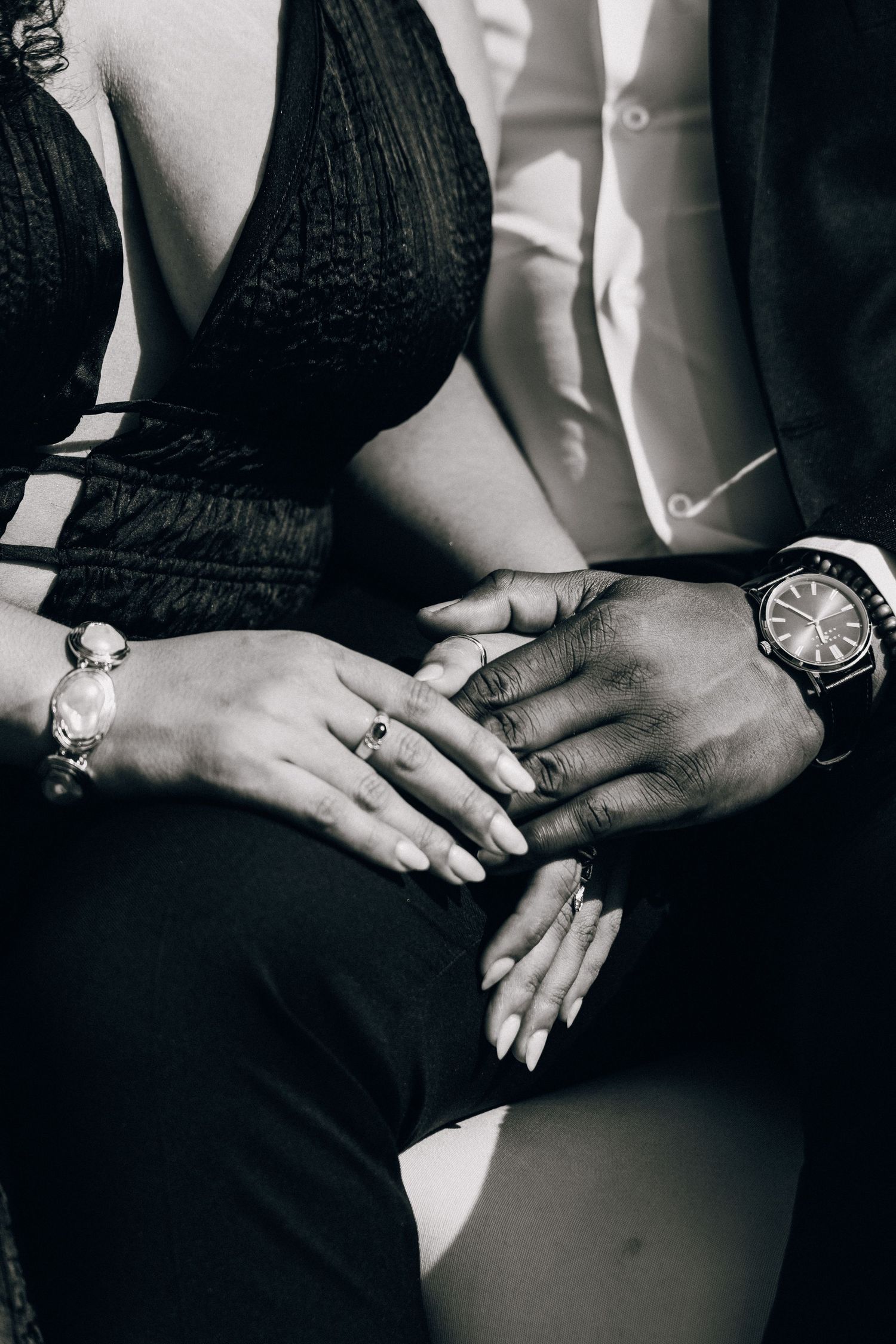 Black and white photo of a couple holding hands, woman wearing rings and bracelet, man wearing a luxury watch.
