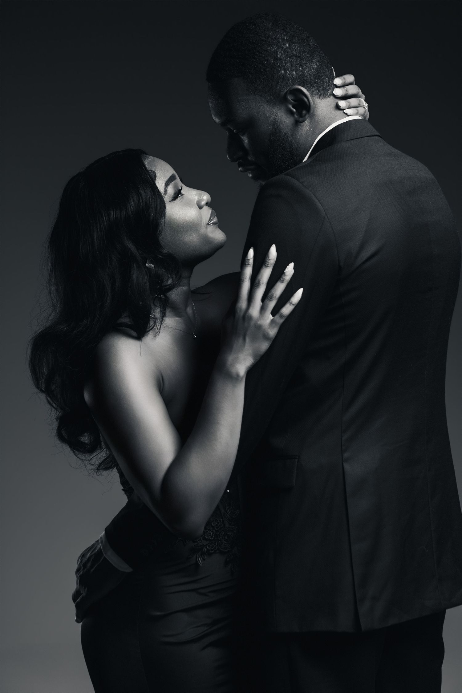 Black and white photo of an elegant couple in formal wear sharing an intimate romantic moment in a studio setting.