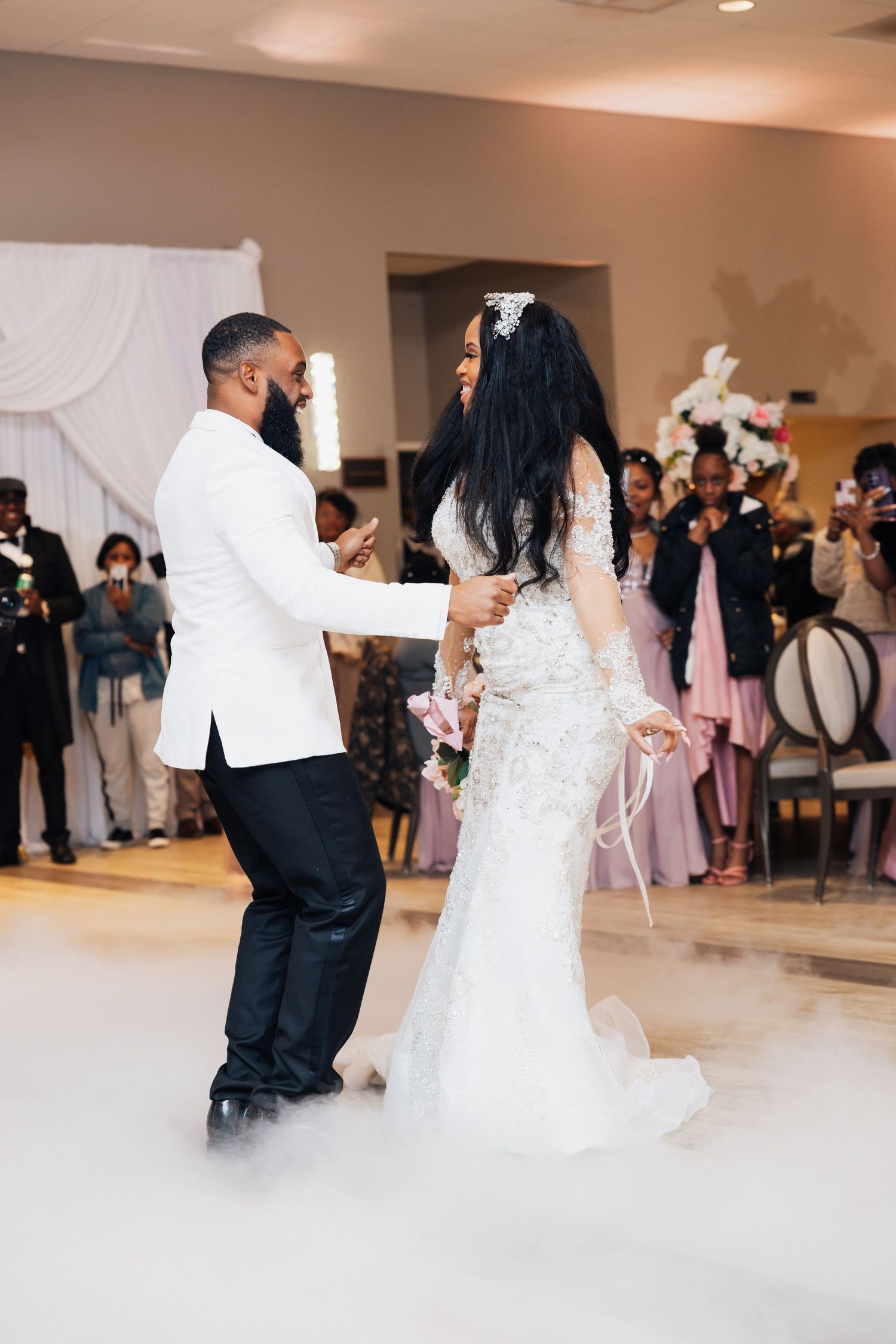 Bride and groom share their first dance surrounded by fog on the dance floor at an elegant wedding reception.