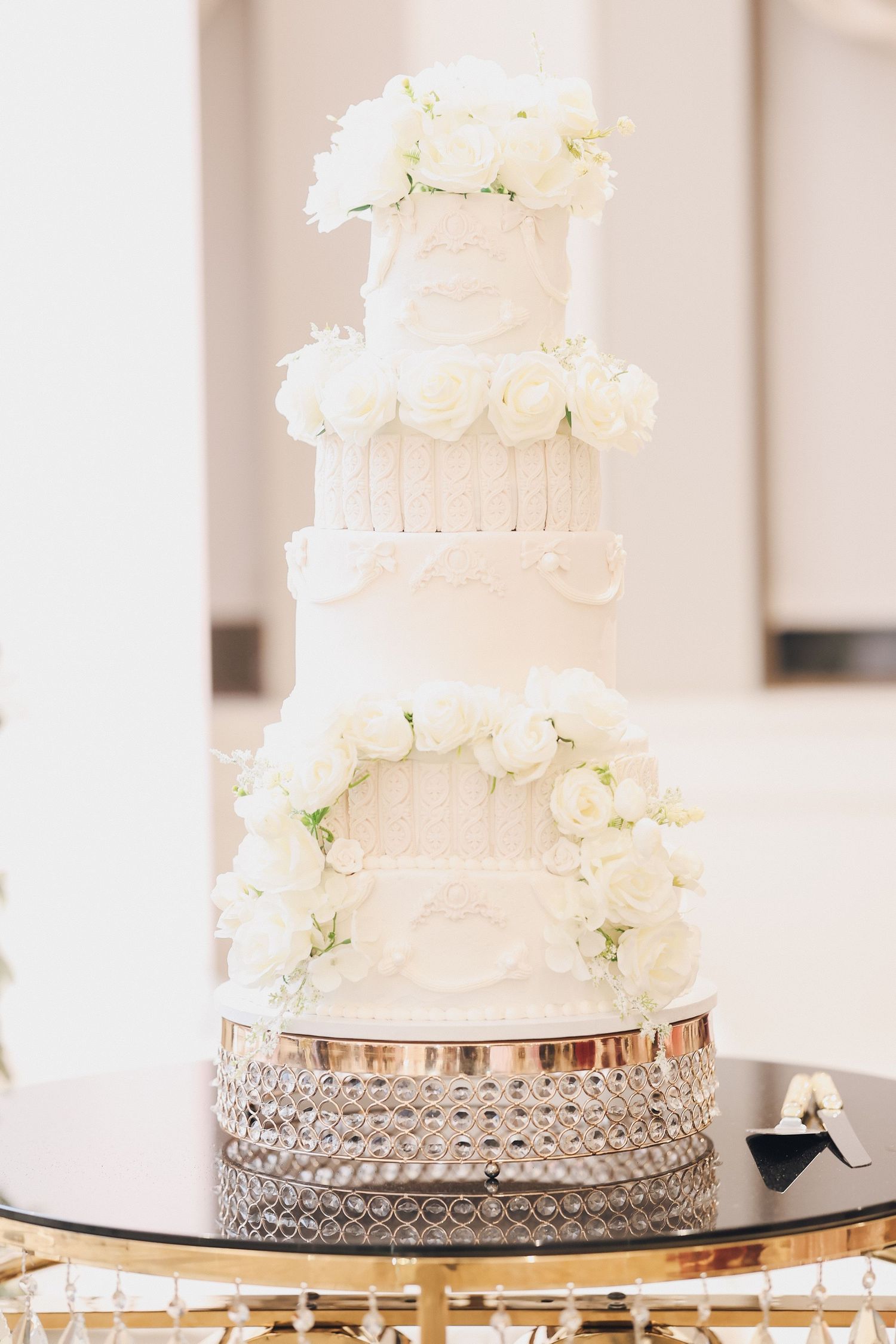 Elegant five-tier white wedding cake with fresh white roses on a crystal stand.