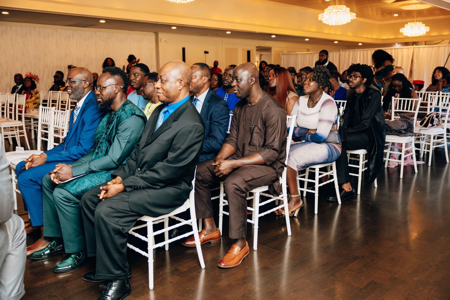 Guests dressed in colorful traditional African attire seated in white chairs at a Nigerian wedding ceremony.
