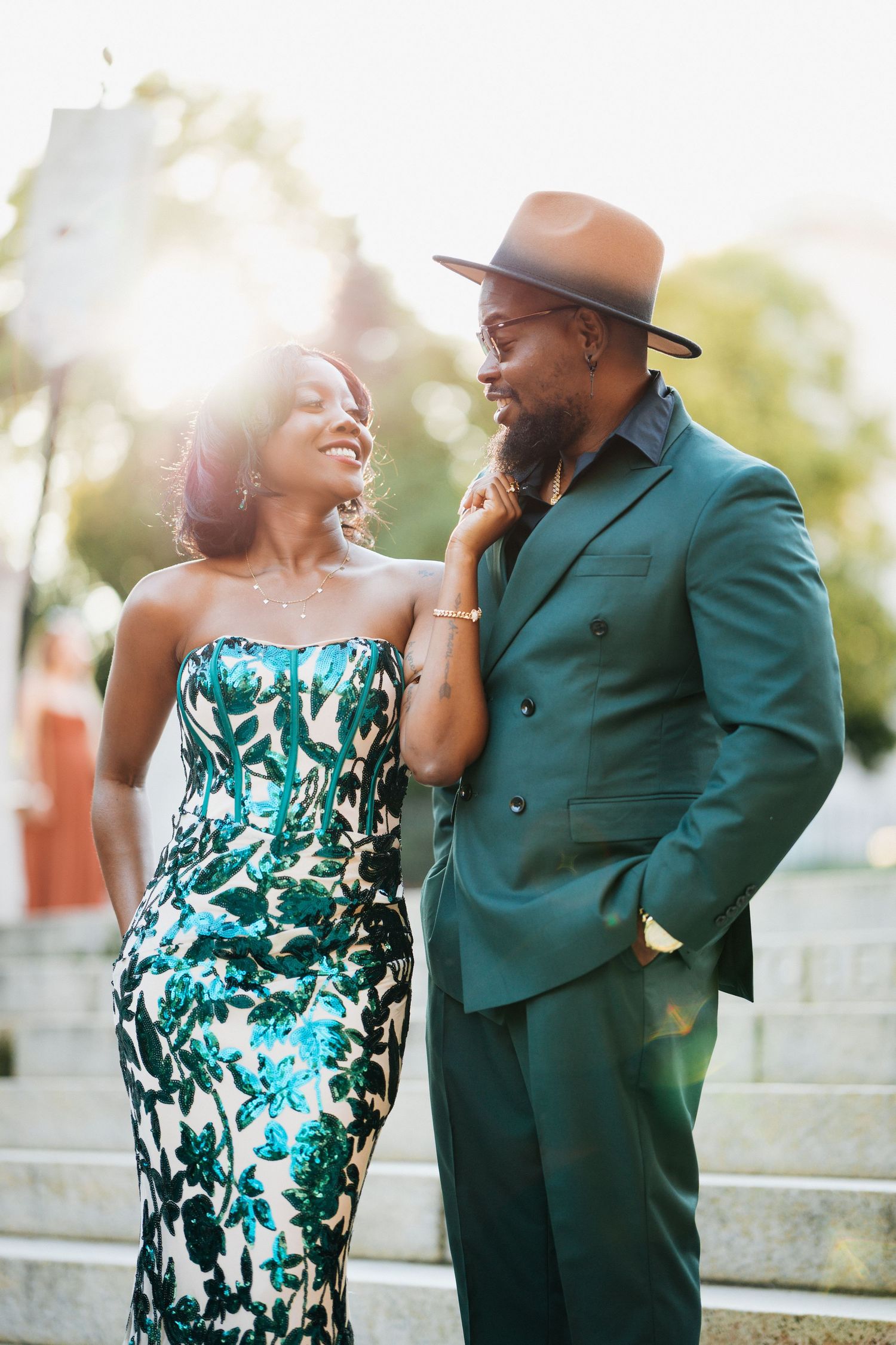 Elegant Black couple in matching emerald green outfits smiling together outdoors in golden sunlight.