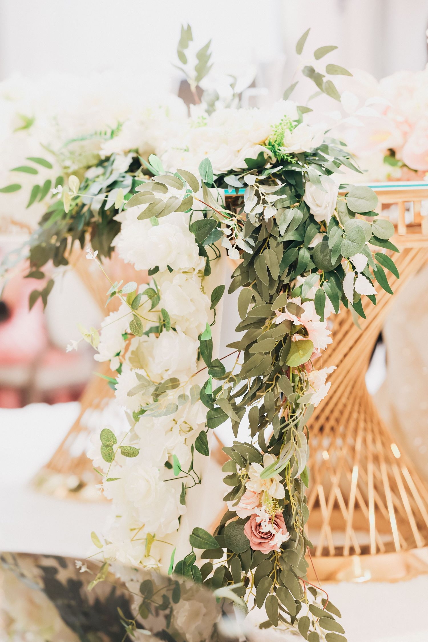 Elegant wedding decor featuring white roses and greenery garland draped over a gold geometric display.