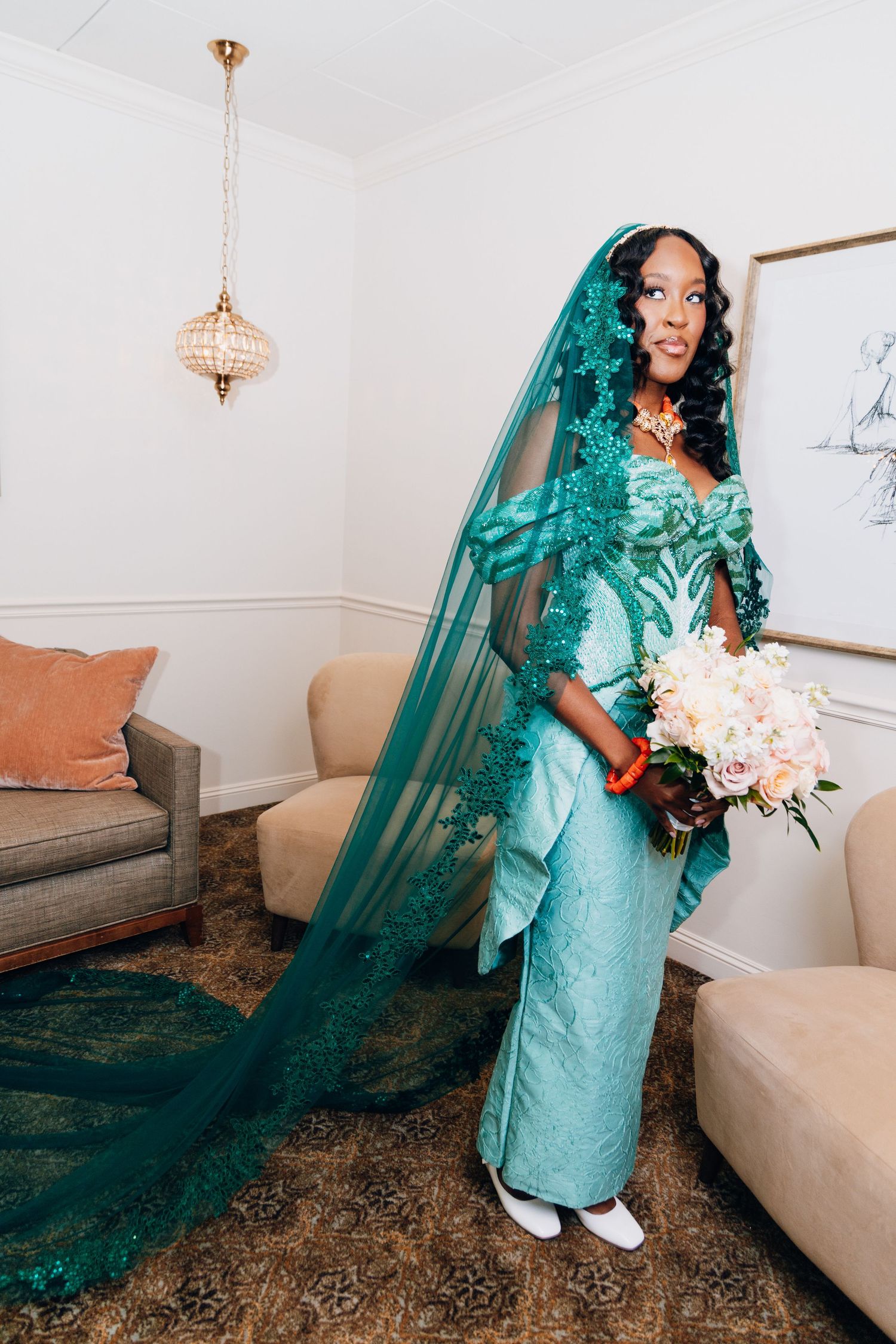 Bride in teal green Nigerian lace wedding attire with matching veil holding blush bouquet.