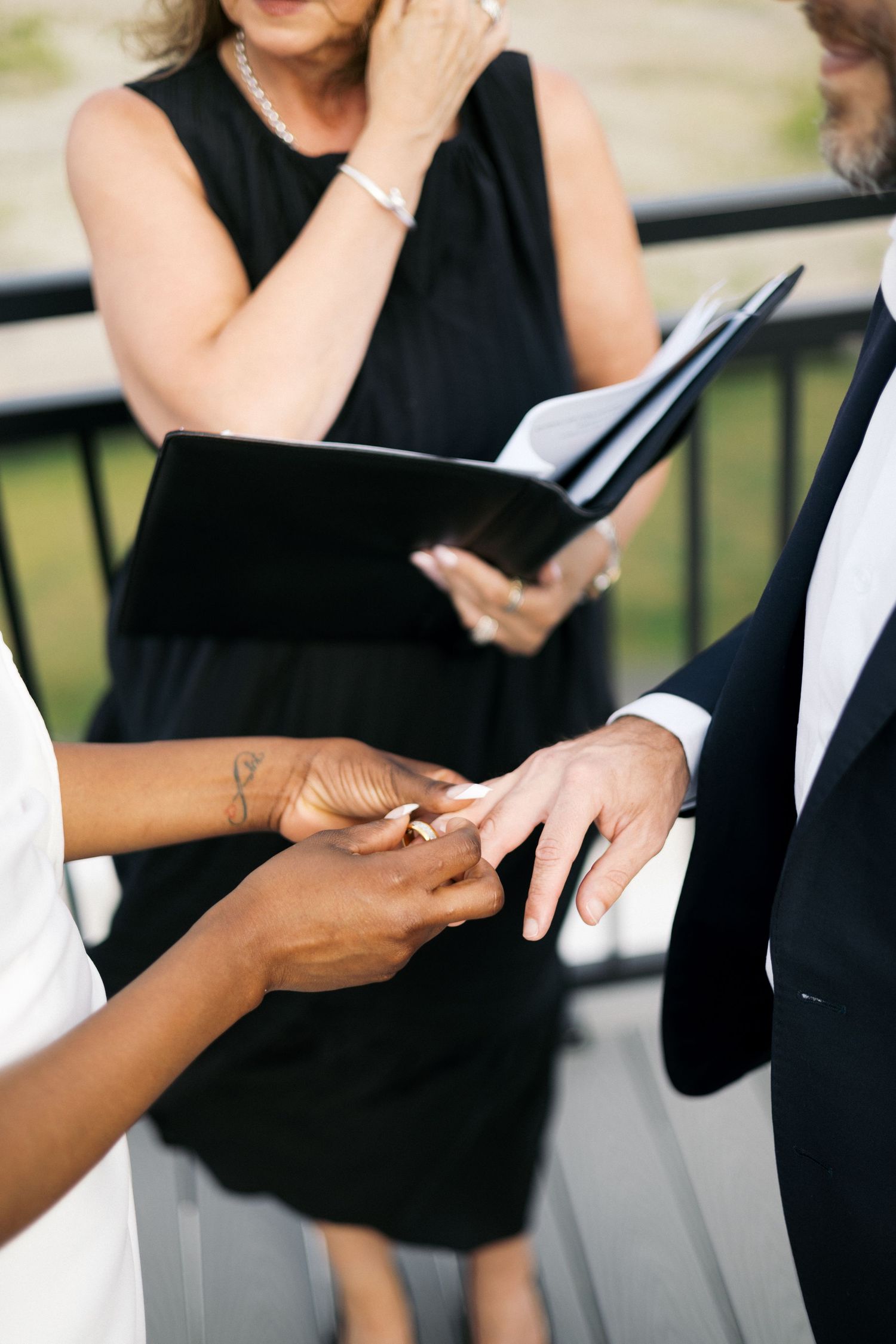 An officiant in black reads vows as an interracial couple exchanges wedding rings during their ceremony.