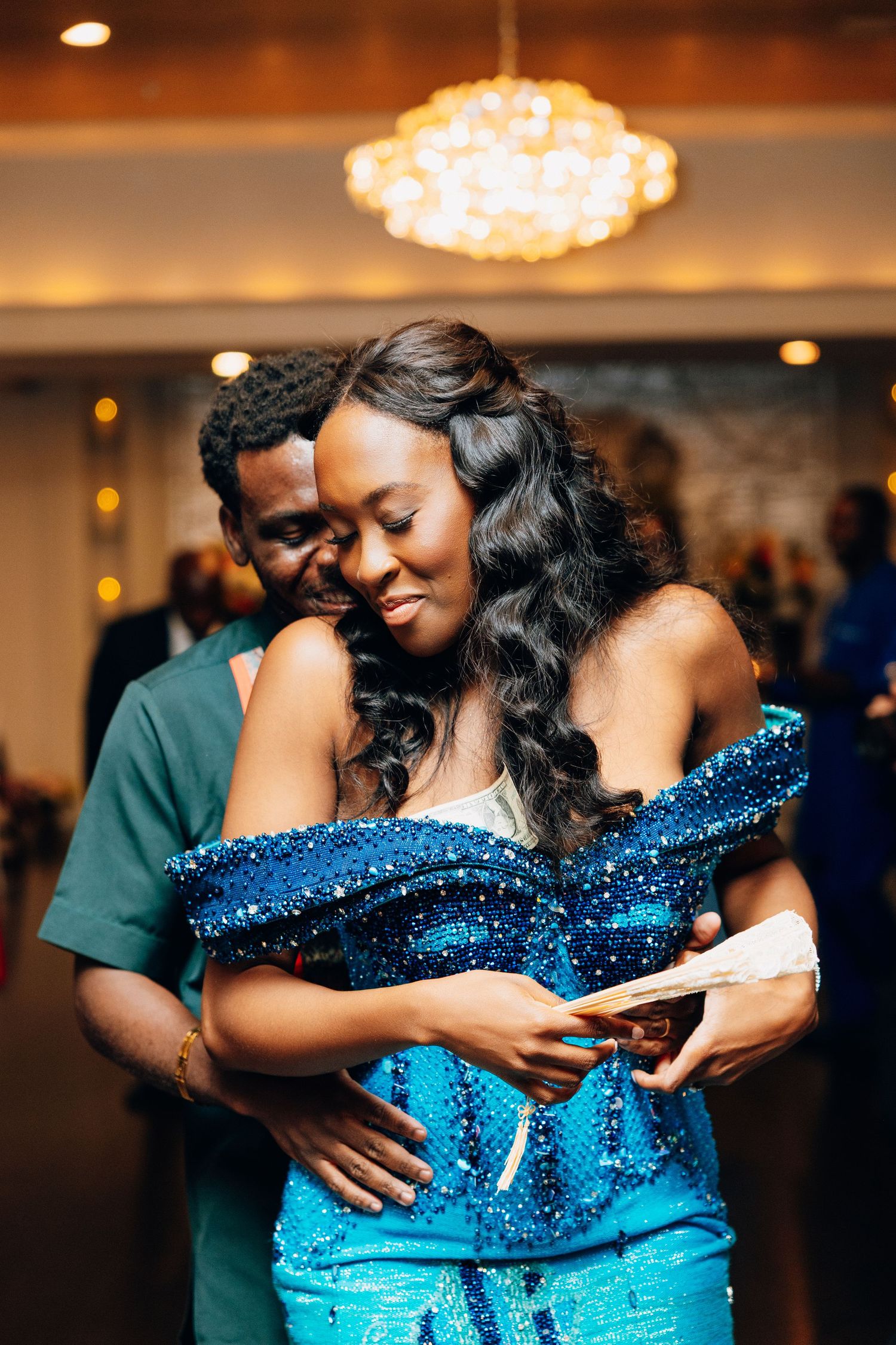 Couple embracing tenderly on dance floor, bride wearing stunning blue sequin gown.
