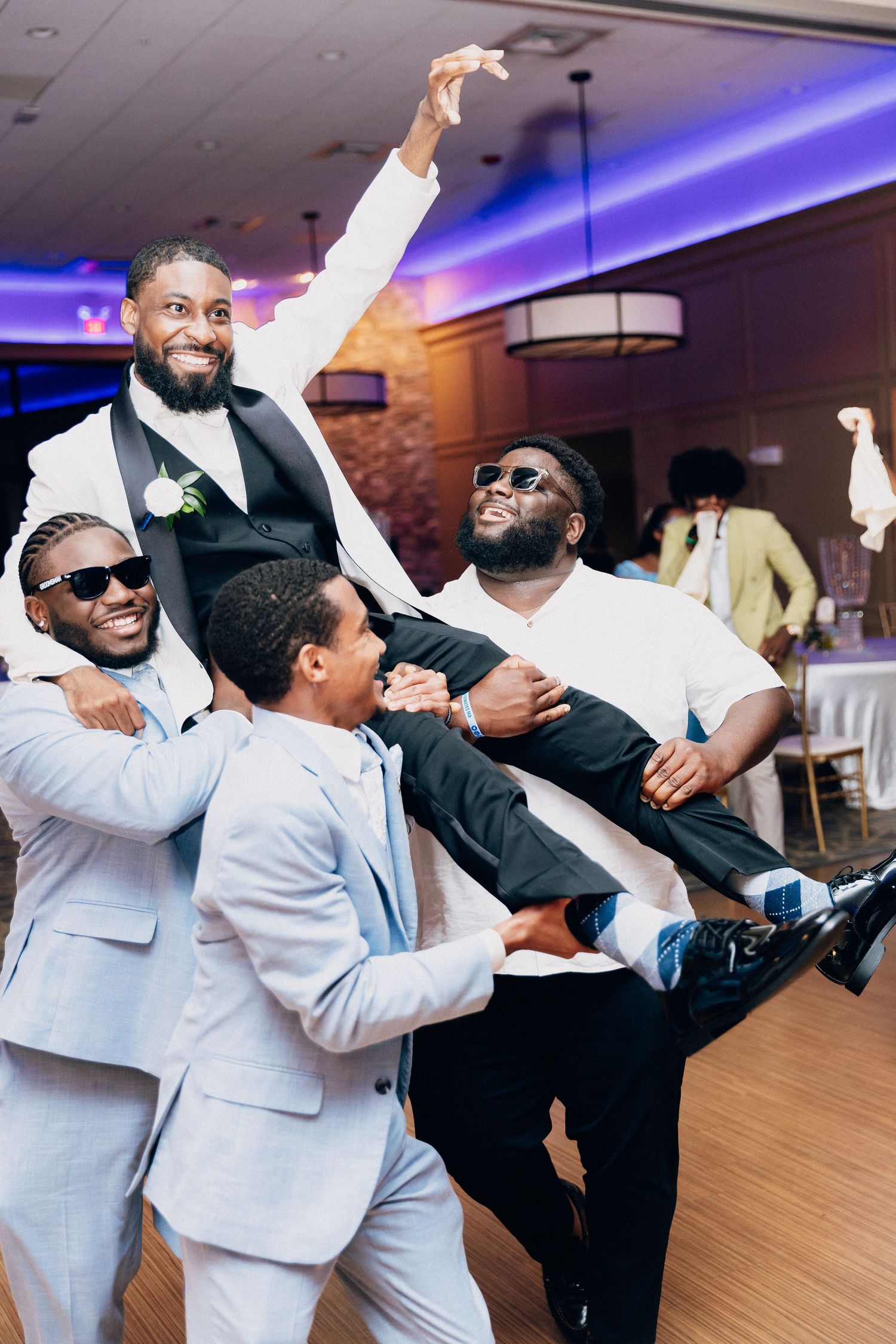 Groomsmen in light blue suits lifting and celebrating the groom on the wedding reception dance floor.