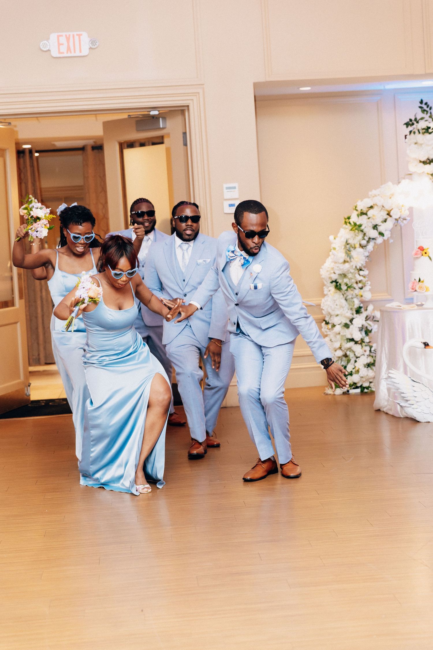 Wedding party in matching light blue attire dancing energetically during fun reception entrance.