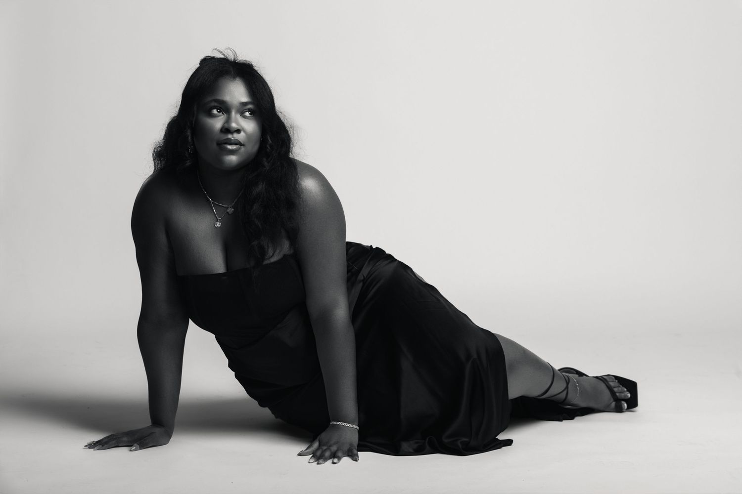 Black and white photo of a woman in an elegant black dress posing gracefully on the floor in a studio setting.