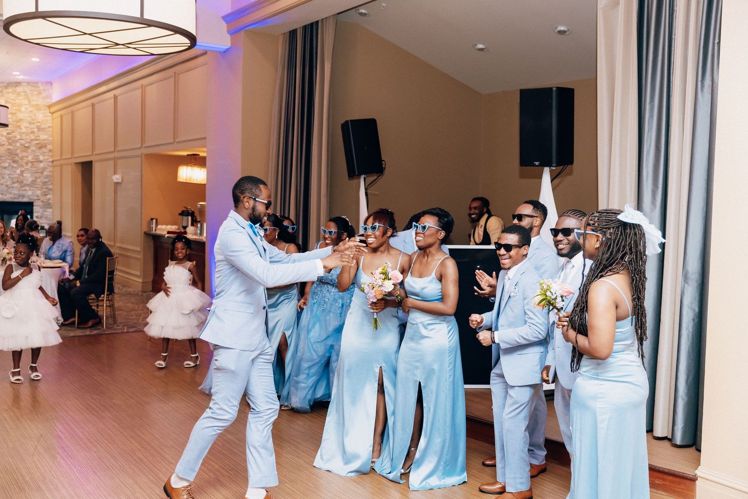 Wedding party in light blue attire dancing joyfully at an elegant indoor reception venue.