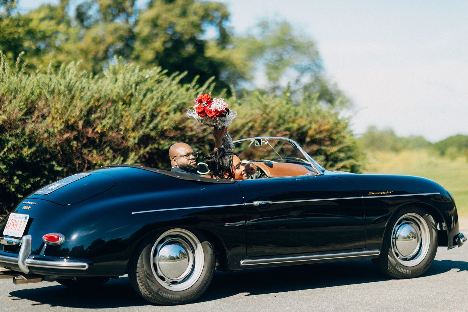 Couple riding in a vintage black Porsche 356 convertible on their wedding day.