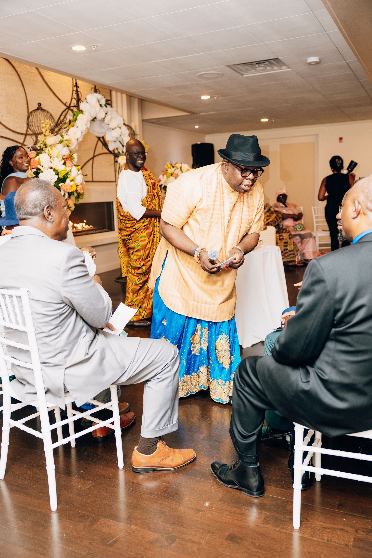 Guests in colorful African attire socialize during a traditional wedding ceremony indoors.