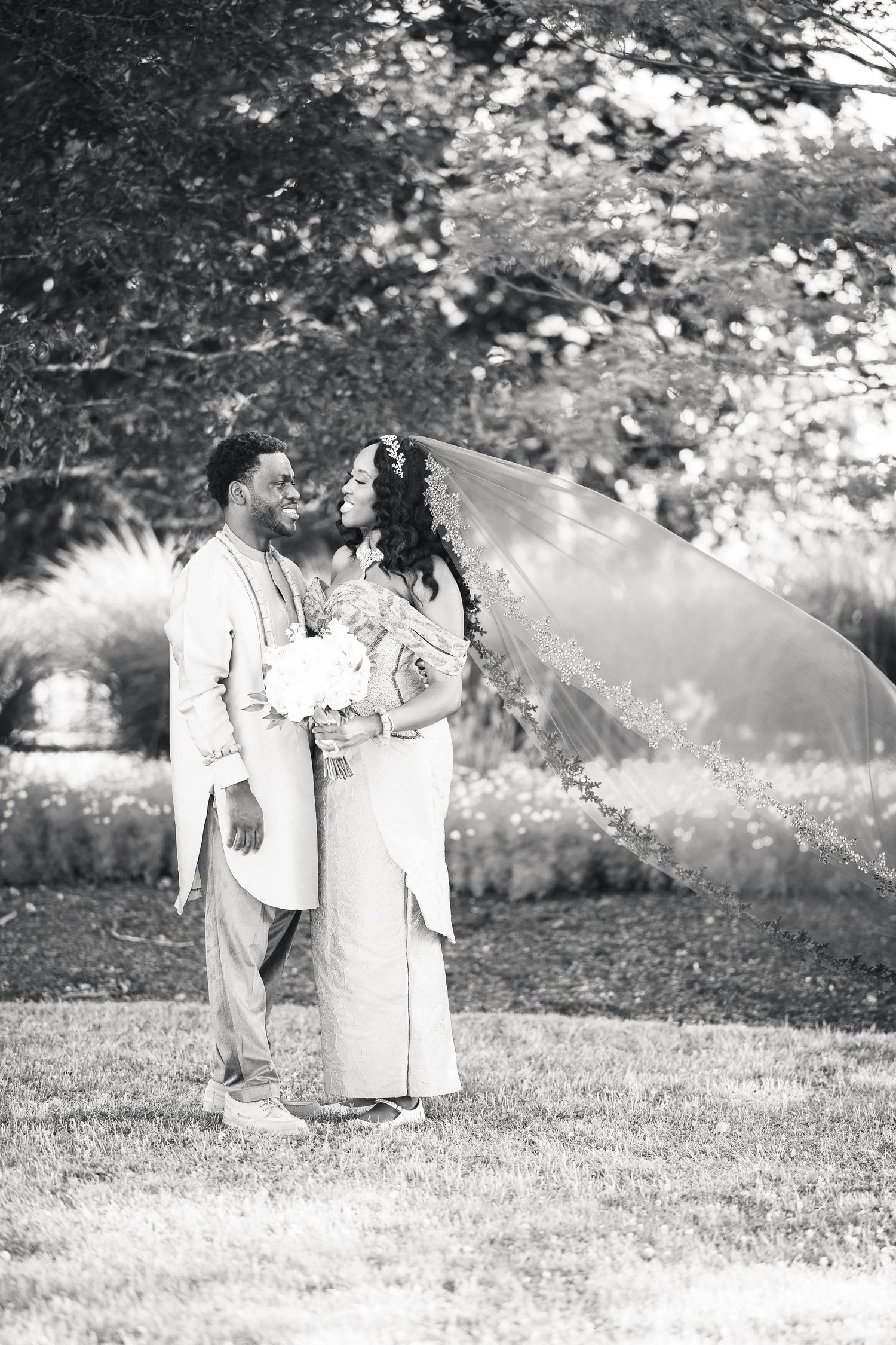 Black and white portrait of bride and groom in traditional African wedding attire outdoors.