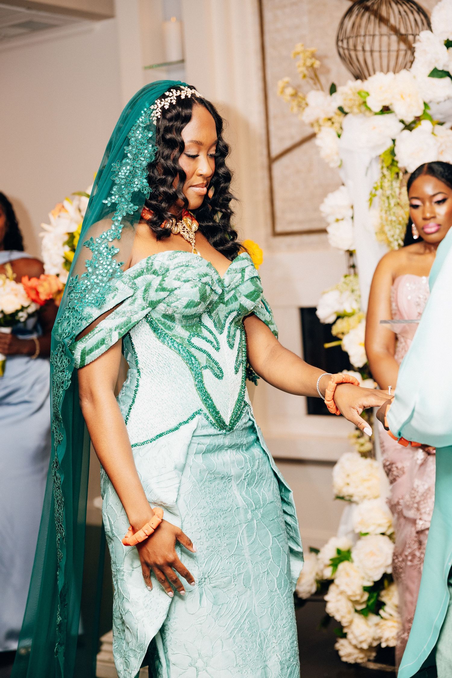 Bride in teal beaded gown with matching veil and orange jewelry at wedding ceremony.