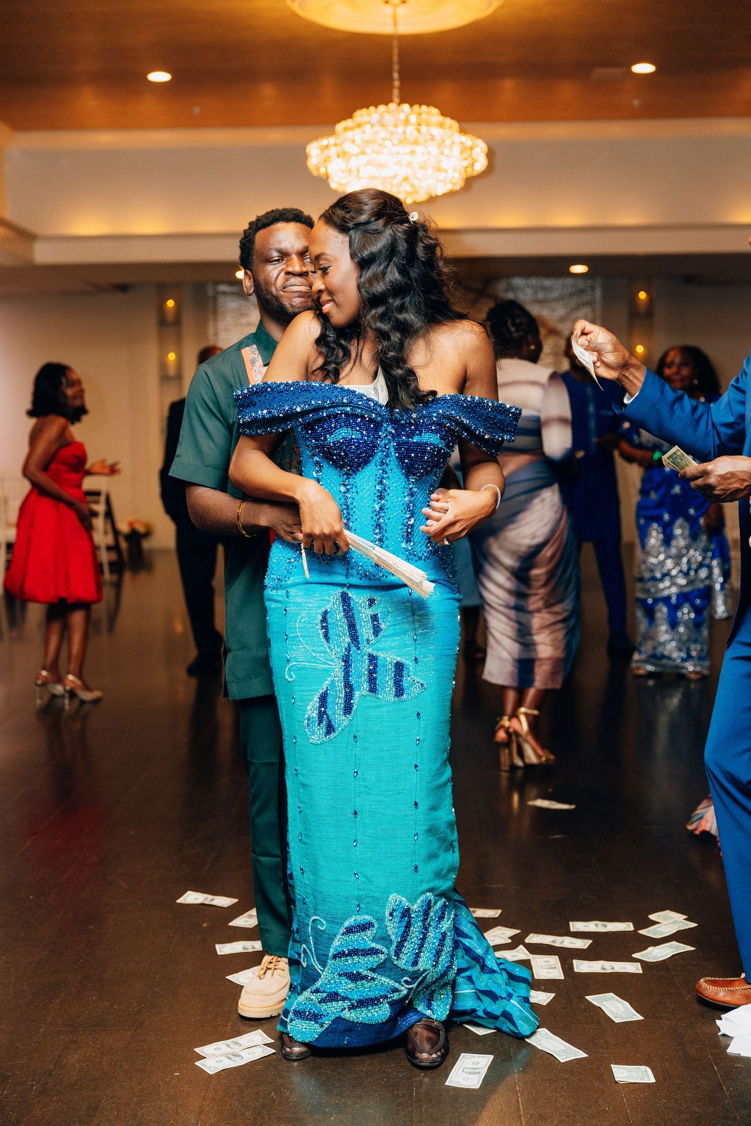 Couple dancing at wedding reception, floor covered in money, bride in blue gown.