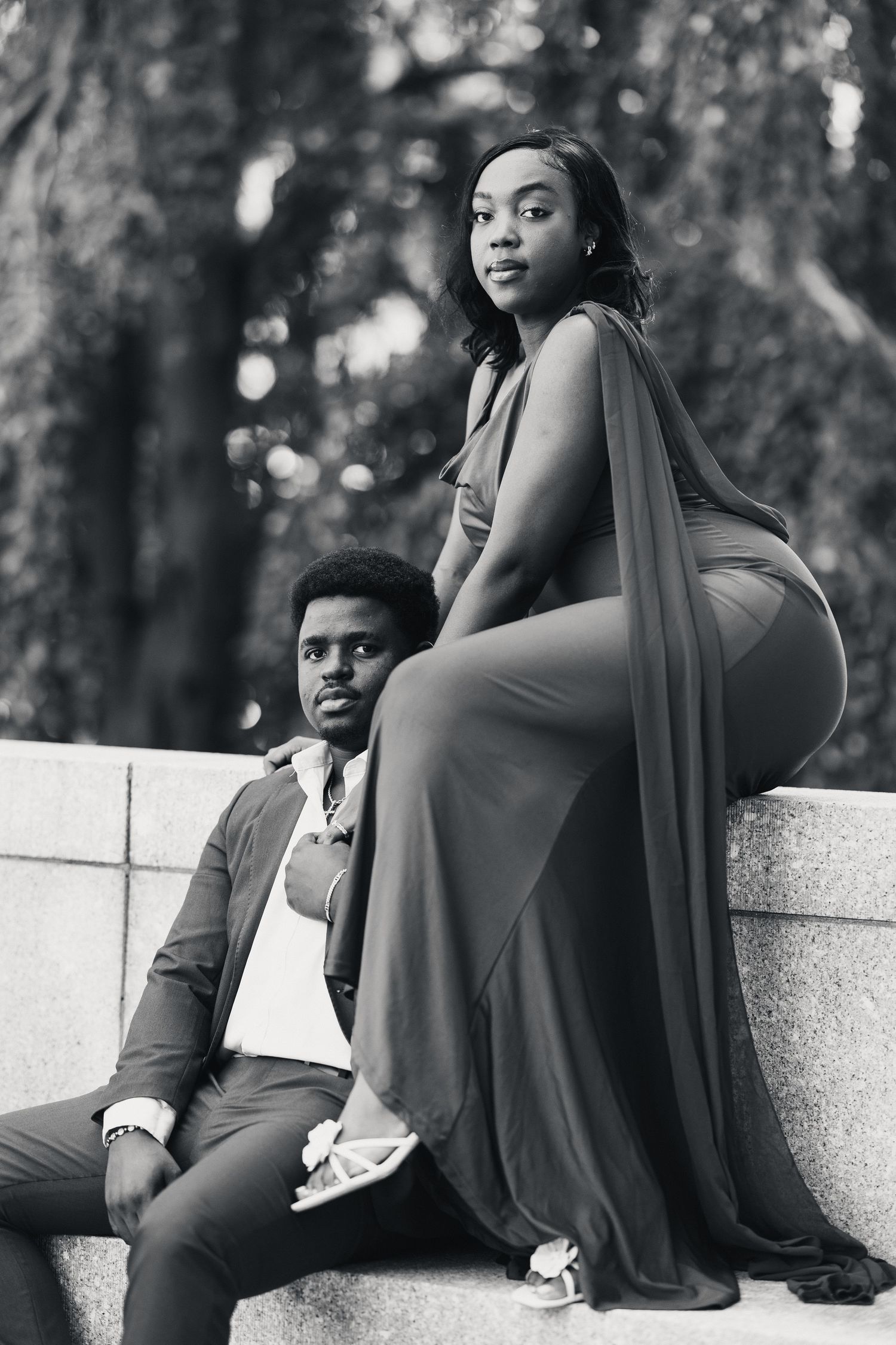Black and white photo of a stylish couple posing on stone steps in a park setting.