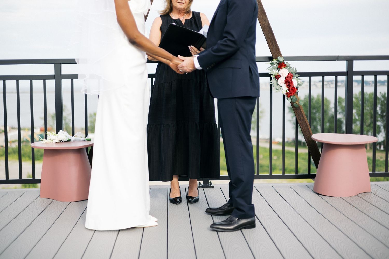 Couple exchanges vows on rooftop deck as officiant in black dress presides over intimate outdoor wedding ceremony.