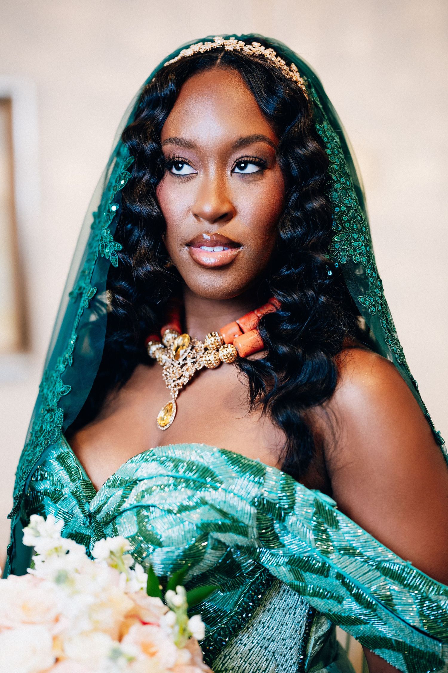 Beautiful African bride in emerald green lace gown wearing coral beaded necklace and gold headpiece.