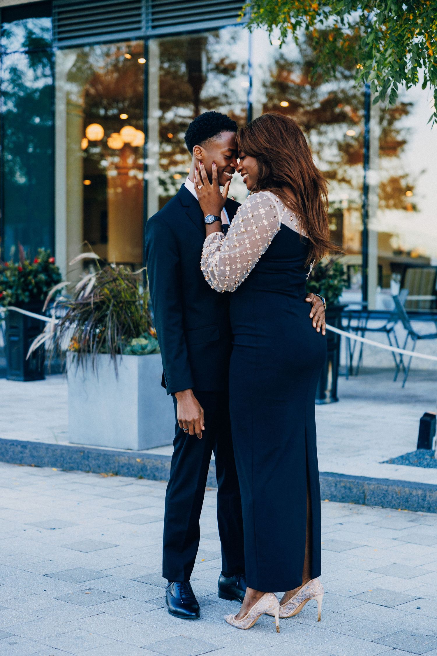 Elegant Black couple in formal attire sharing a romantic moment outdoors near a modern building.