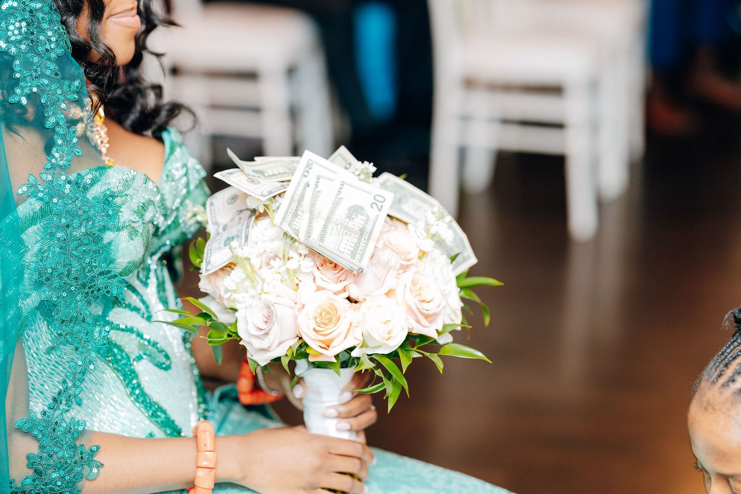 Bride holds white rose bouquet decorated with dollar bills during African wedding ceremony.