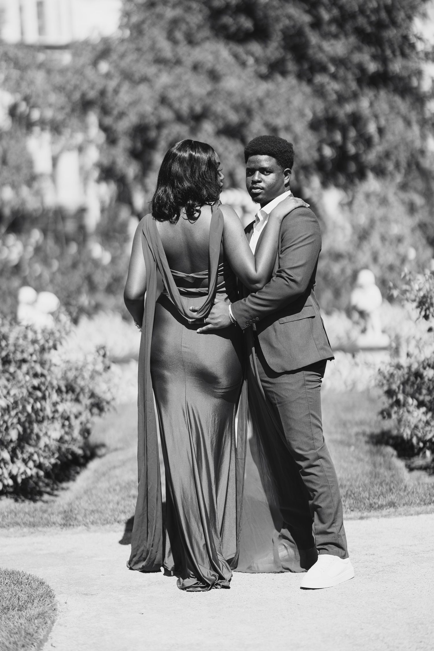 Black and white photo of an elegant couple in formal wear standing in a garden.