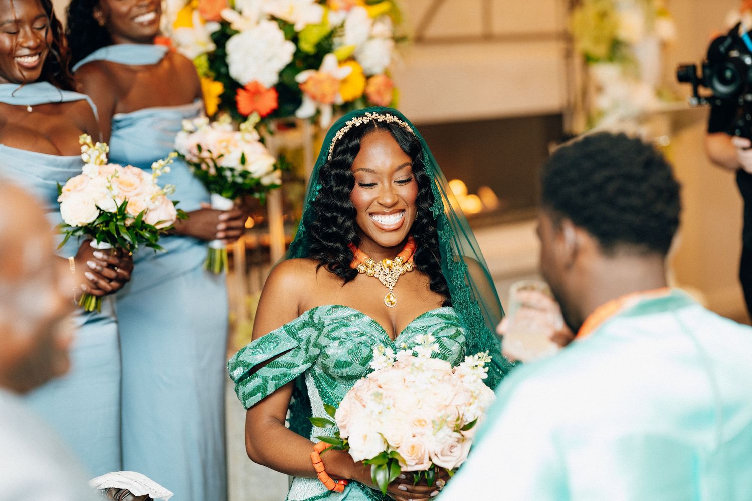 Radiant bride in teal gown and veil smiling with bridesmaids in blue dresses.