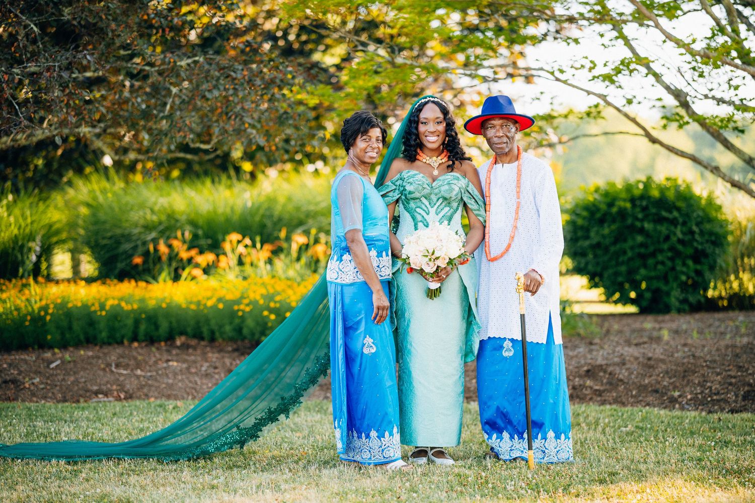 Three women in elegant blue and green African attire pose outdoors at a wedding celebration.