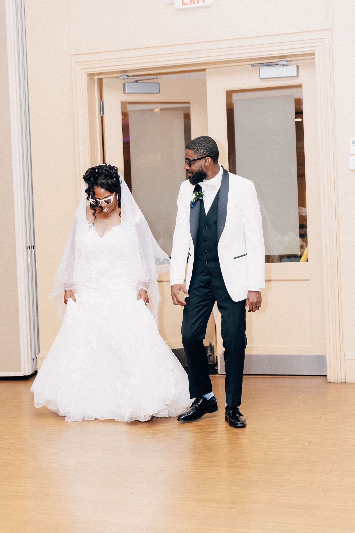Bride in white gown and groom in white tuxedo jacket walking hand in hand at wedding venue.