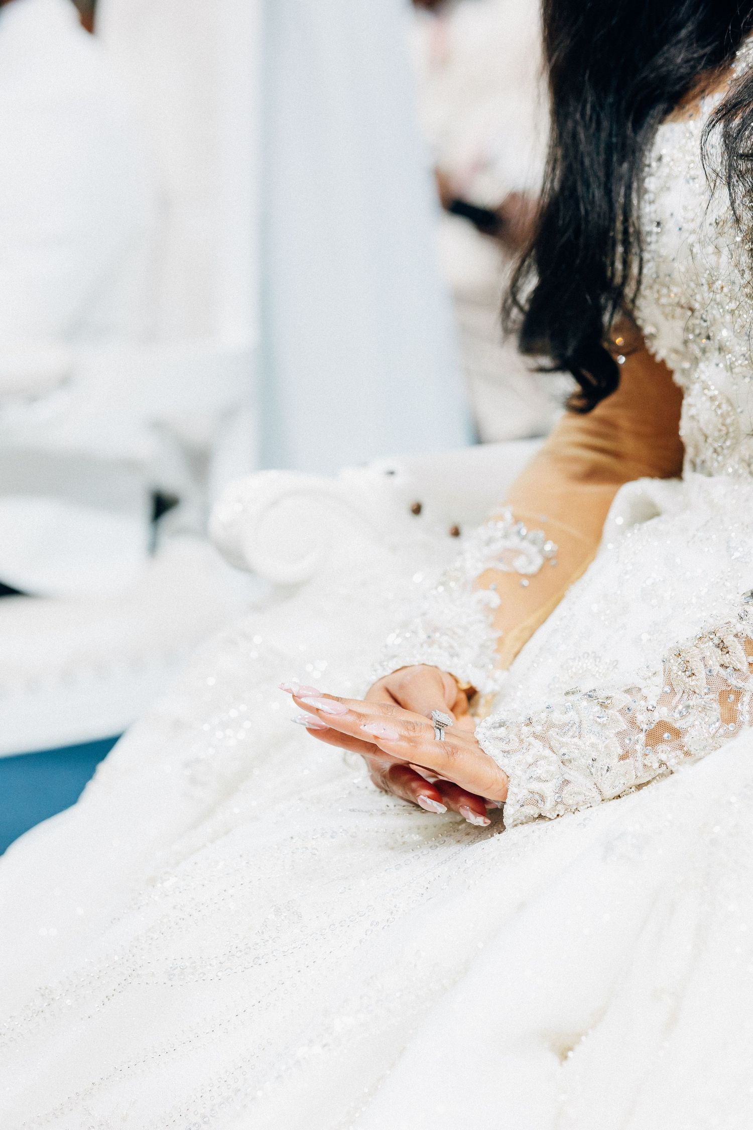 Bride in elegant white lace wedding gown with intricate beading seated and holding a smartphone.