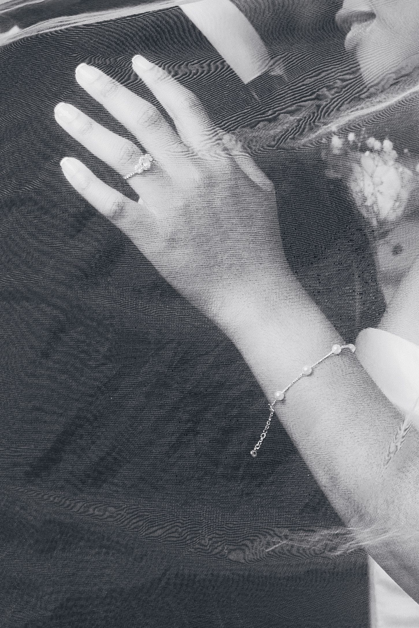Close-up black and white photo of a bride's hand with diamond engagement ring and delicate bracelet resting on groom's suit.