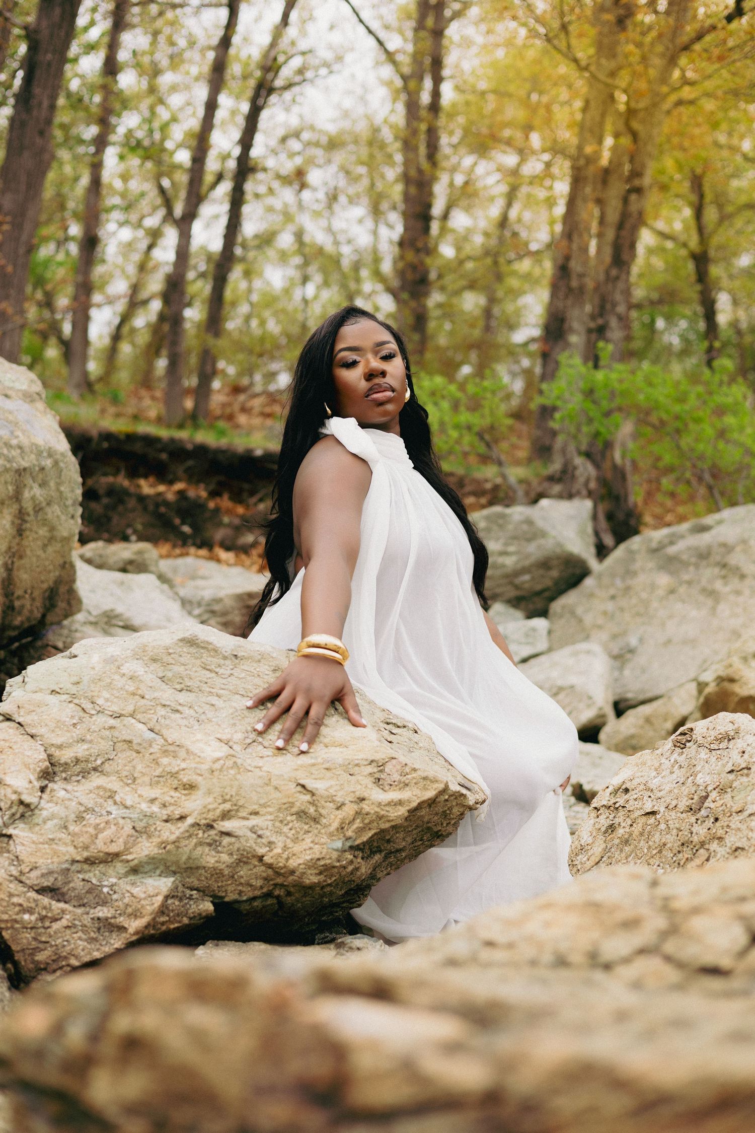Woman in white dress posing gracefully on rocky terrain surrounded by autumn trees in a serene forest setting.