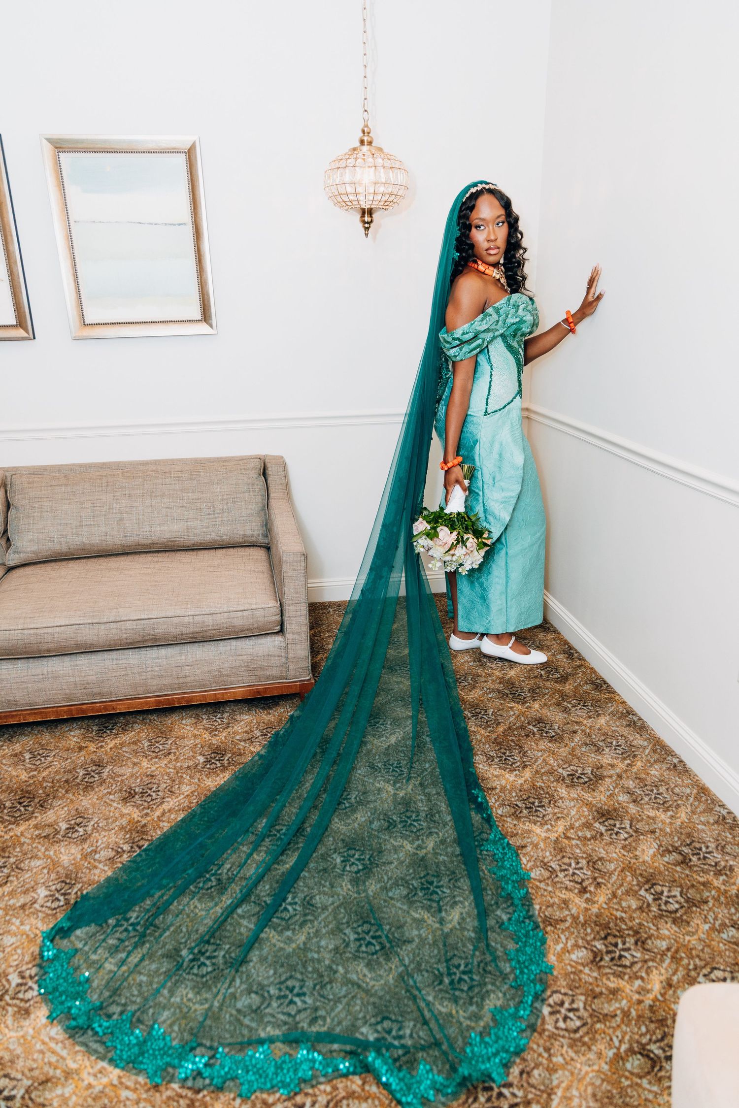Black bride in teal sequined gown with dramatic floor-length lace veil holding white bouquet in elegant room.