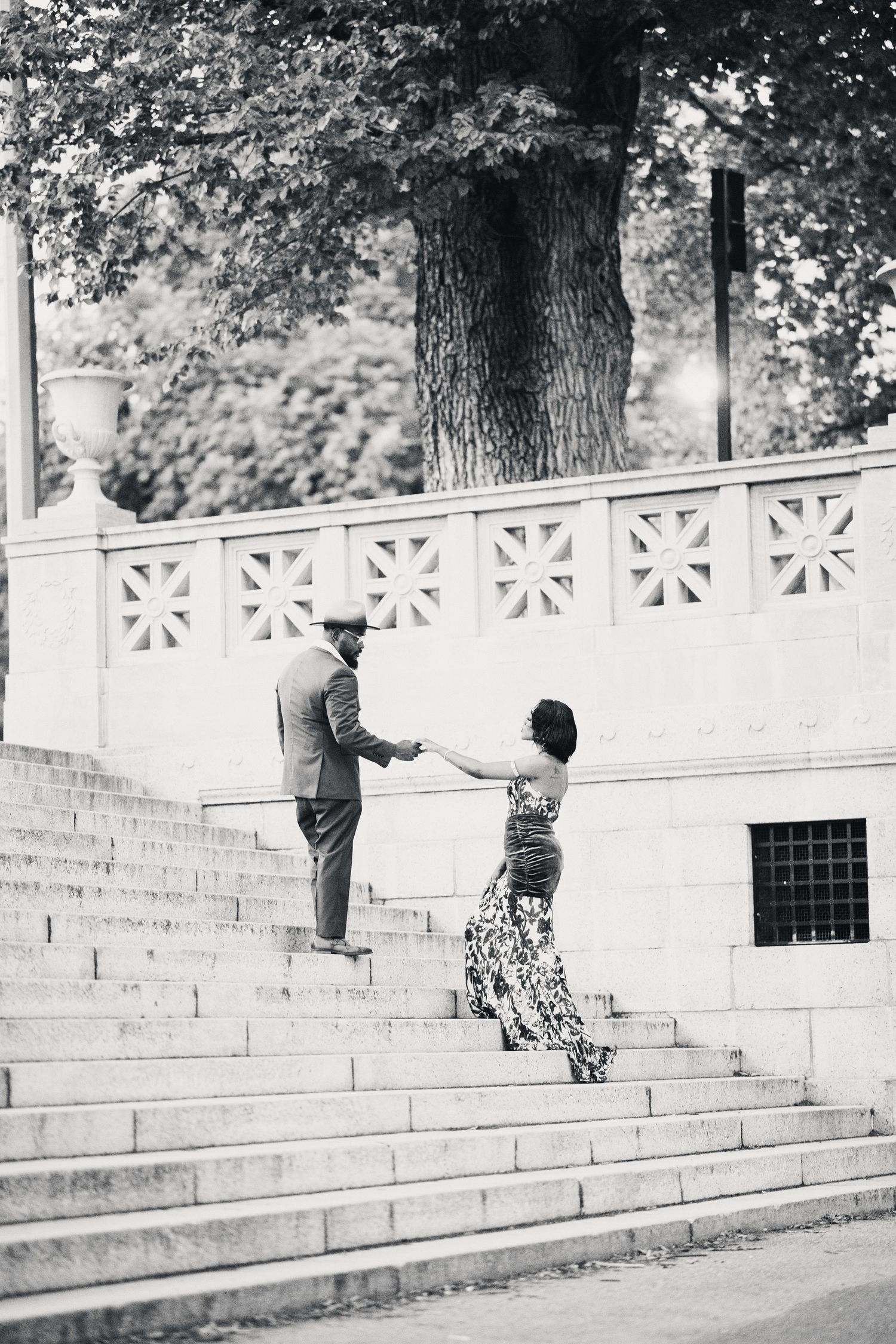 Black and white photo of an elegant couple holding hands while climbing ornate stone steps in a park.