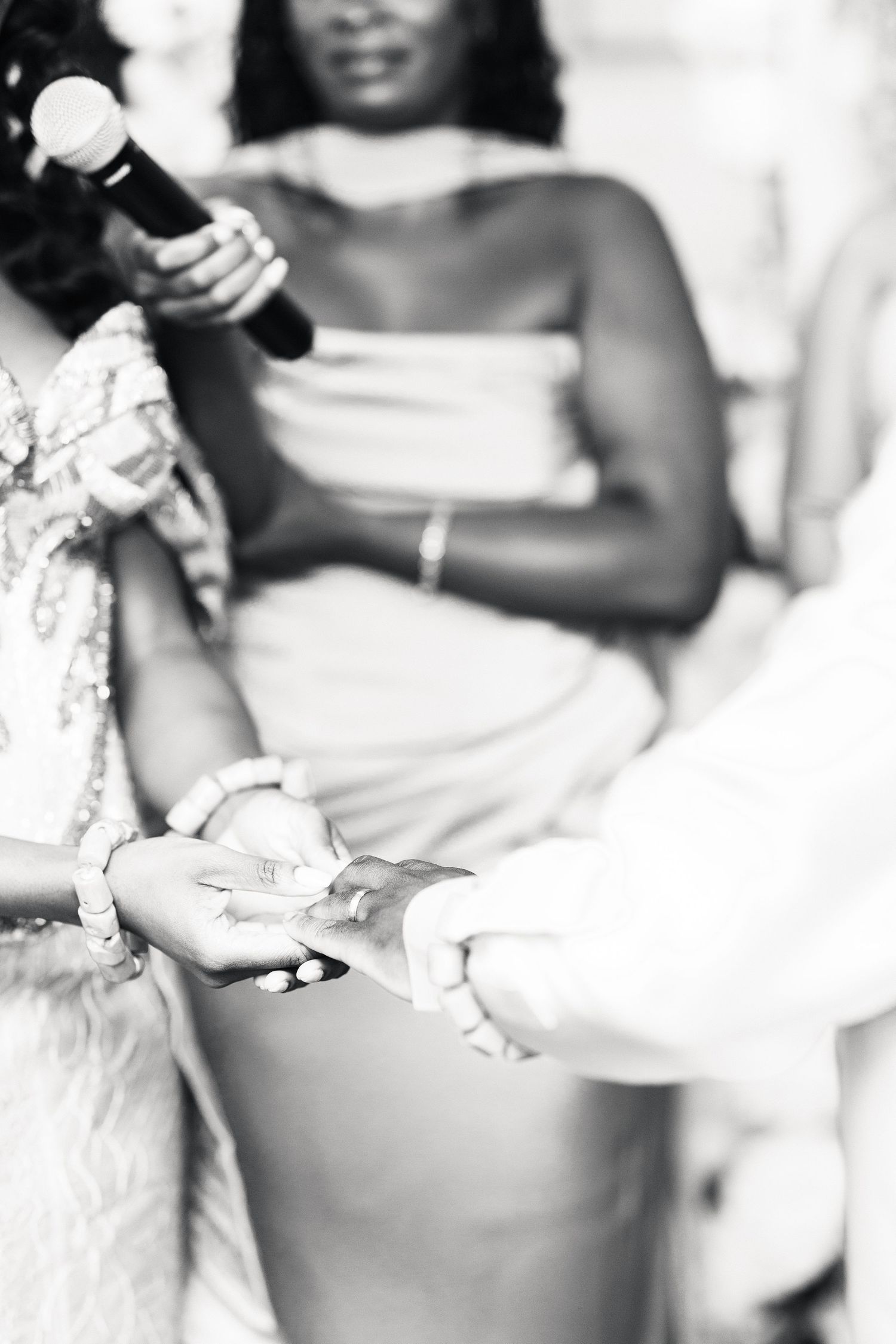 Black and white photo of ring exchange during African wedding ceremony with guests in background.