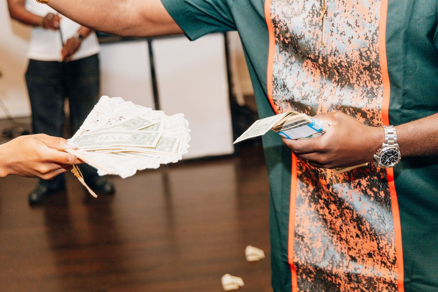 Two people exchanging cash money at an indoor event, with one person wearing a patterned shirt and silver watch.
