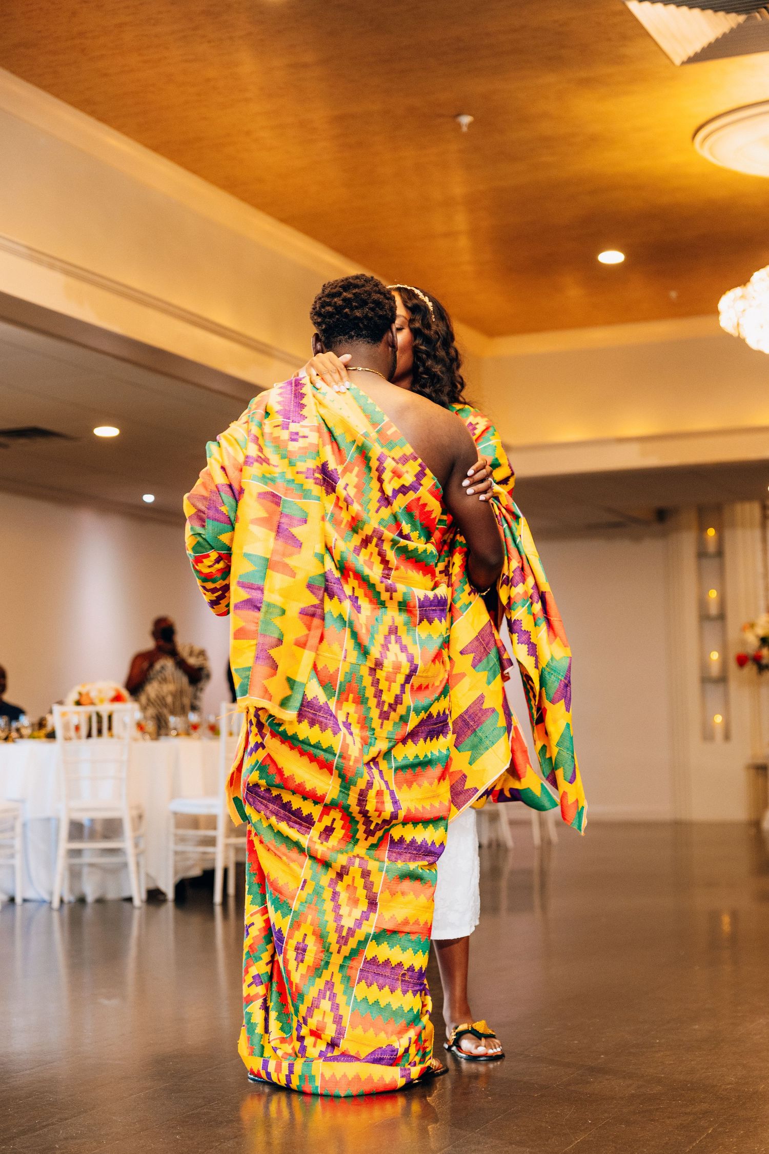 Couple sharing first dance wrapped in colorful Kente cloth at wedding reception.