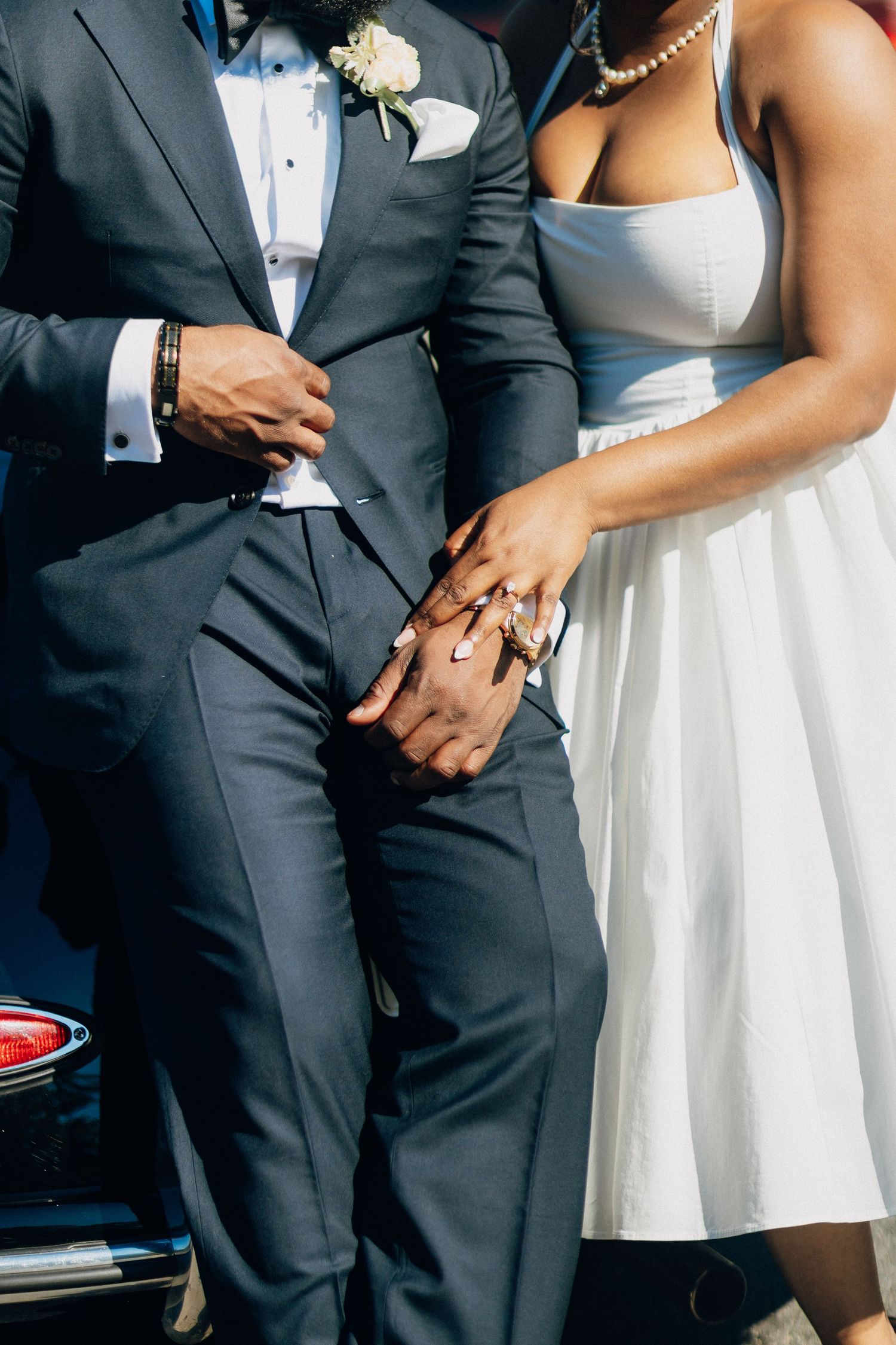 Newlyweds holding hands showing wedding rings, bride in white dress groom in navy tuxedo.