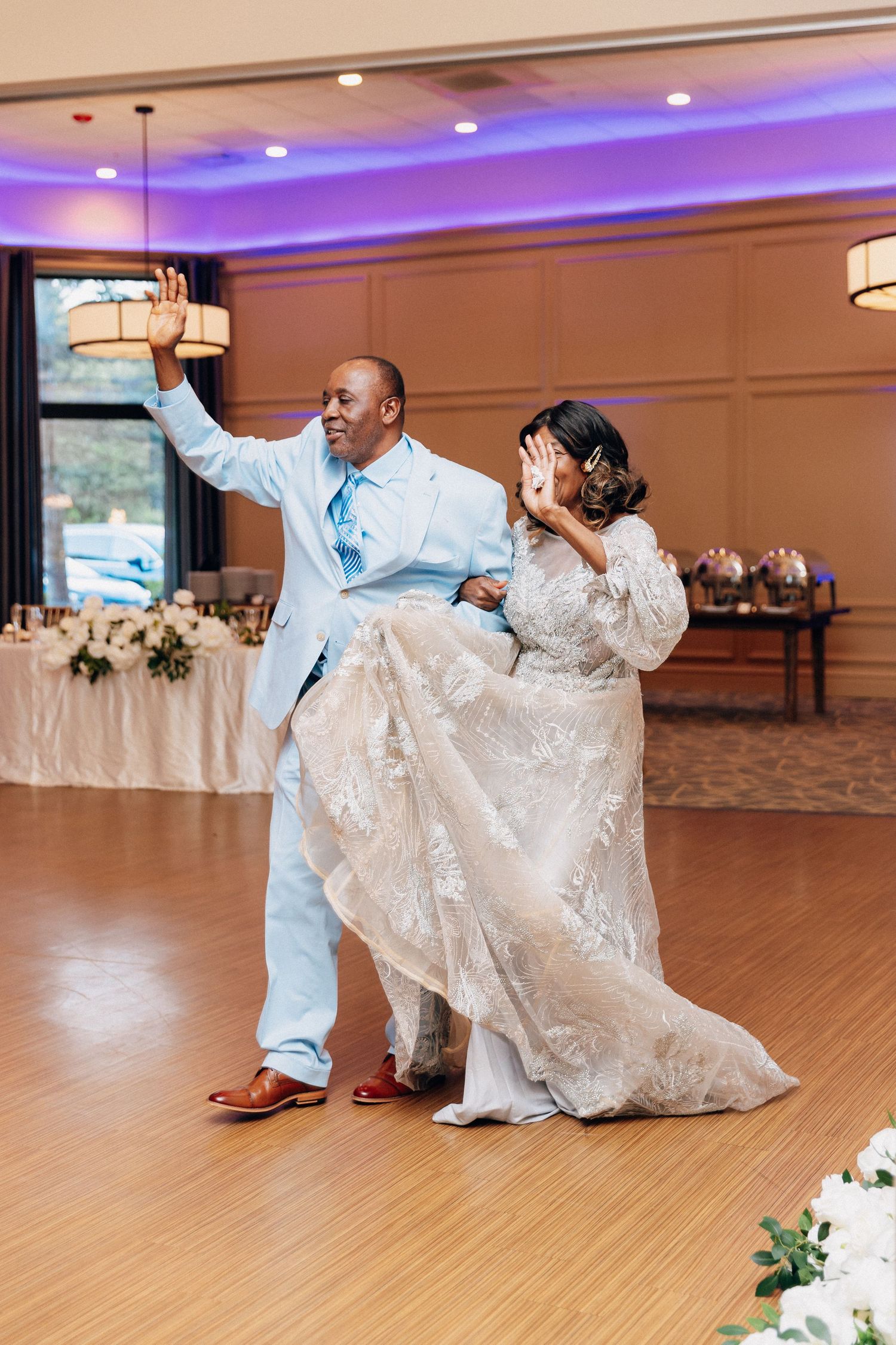 Bride and groom sharing joyful first dance in ballroom with purple uplighting at wedding reception.