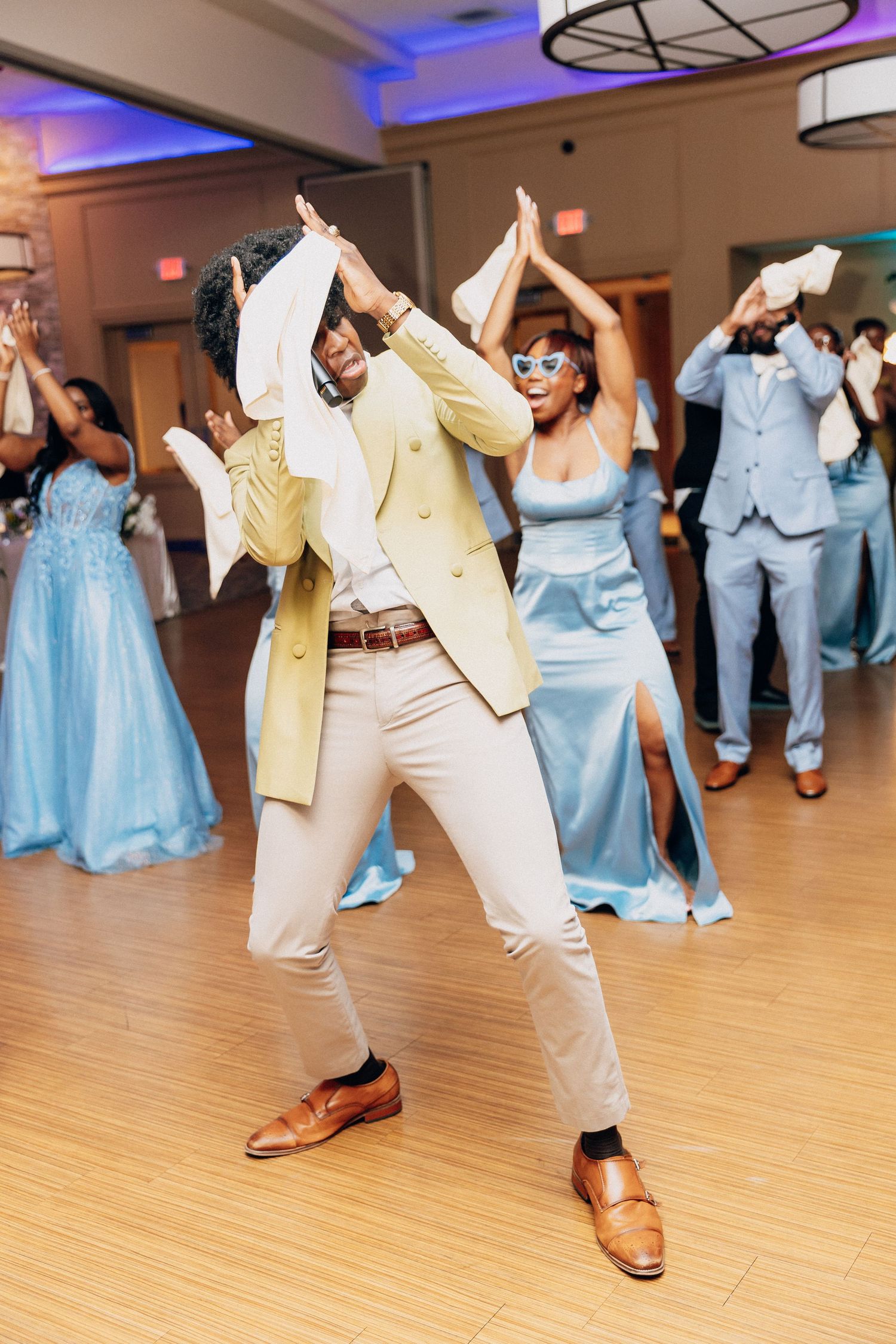 Guests dancing joyfully at a wedding reception in blue and yellow formal attire on a wooden dance floor.