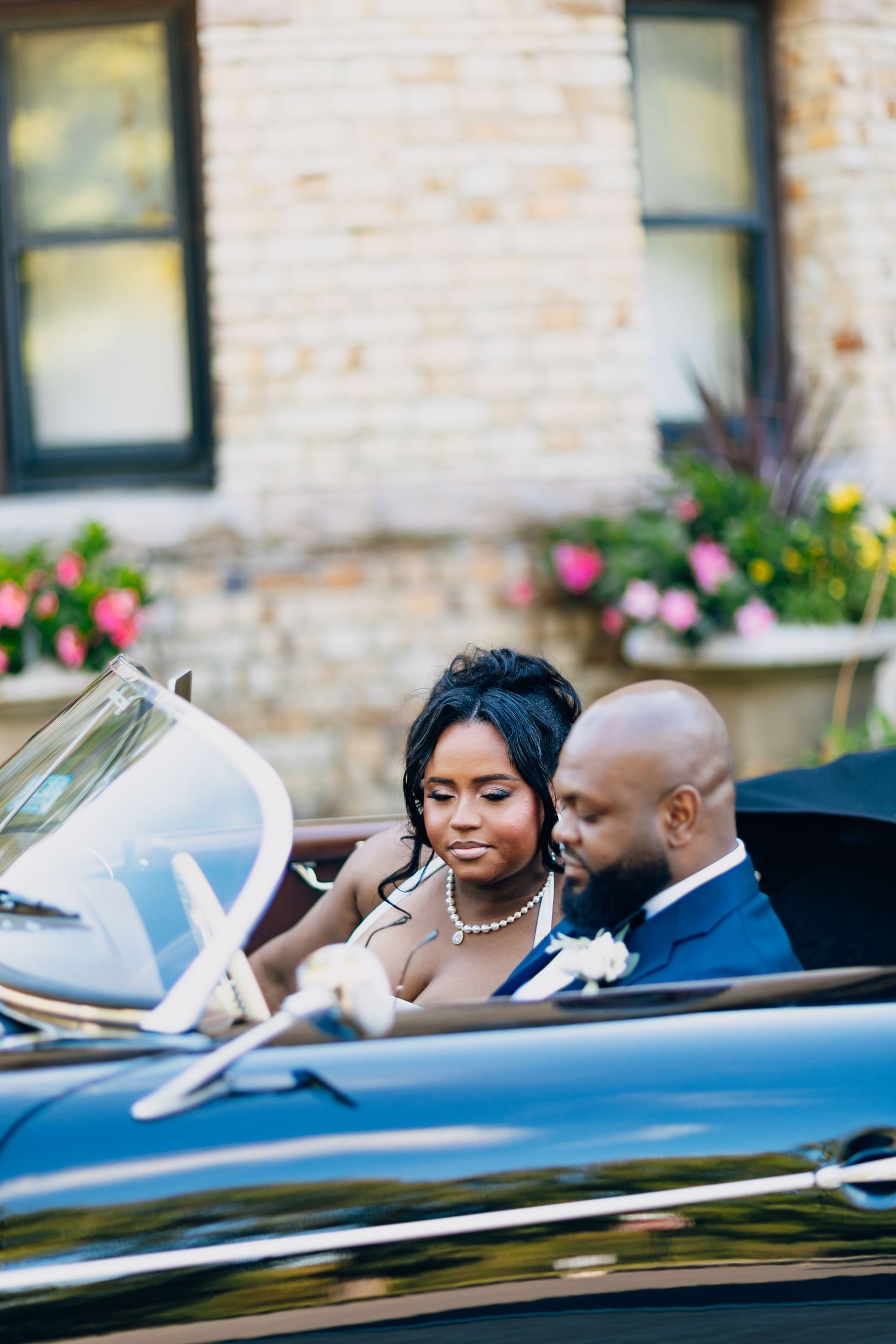 Elegant Black bride and groom sit closely together in a vintage convertible car on their wedding day.