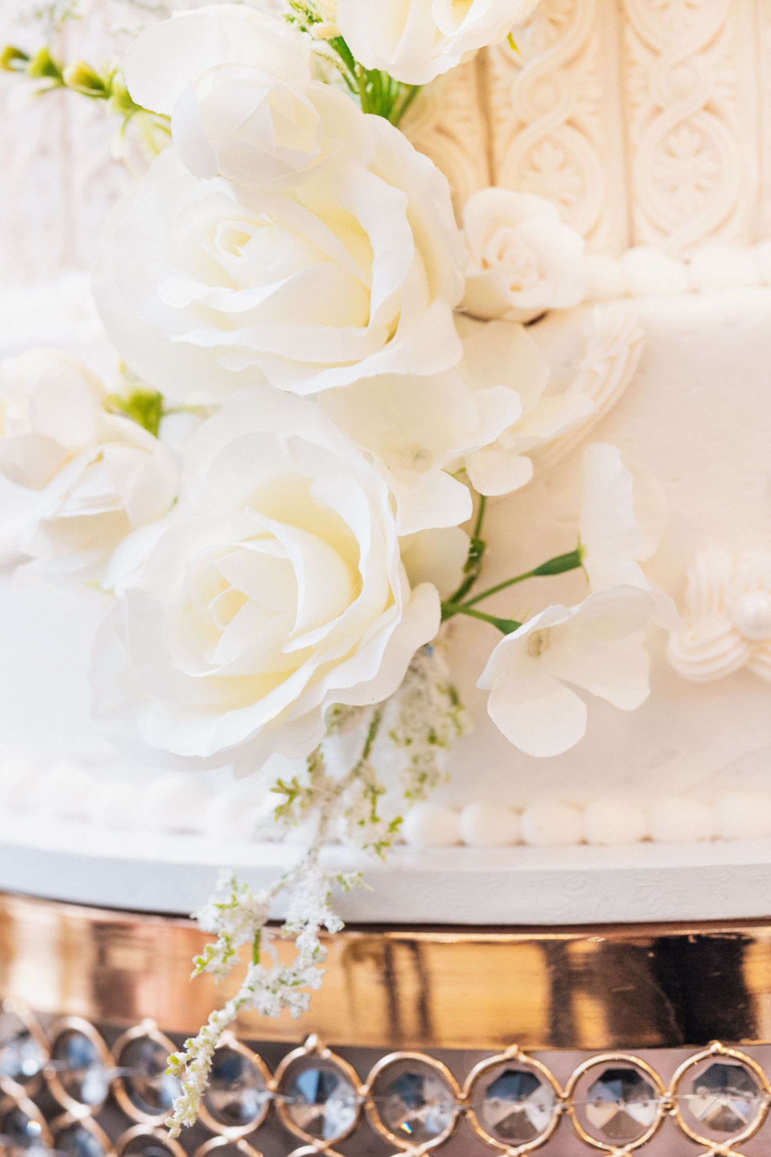 White wedding cake with elegant sugar roses and floral decorations on a crystal cake stand.